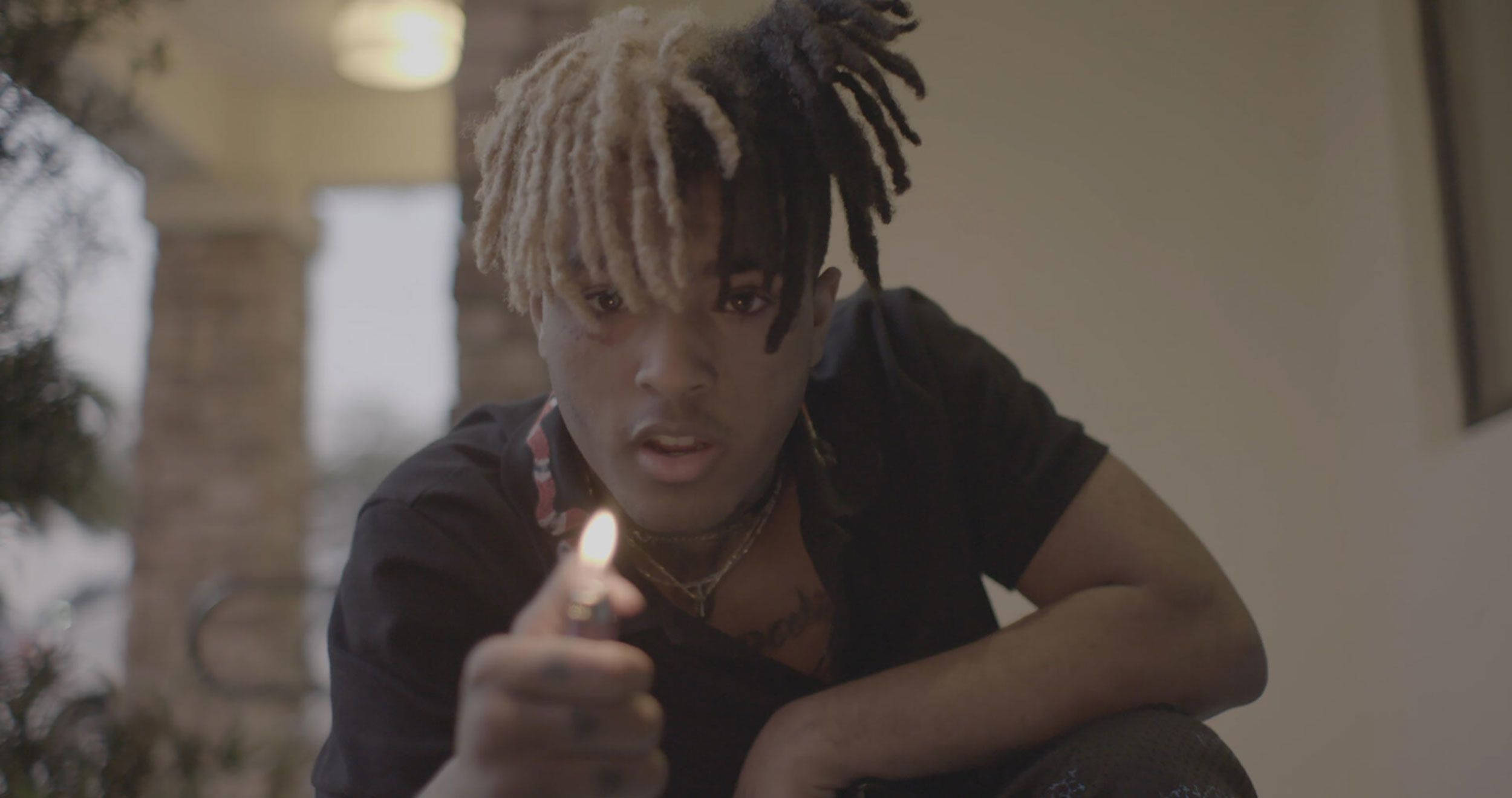 xxxtentacion 電腦 桌布 壁紙 — 一位擁有雙色辮子辮的年輕男子在室內蹲下，手持點燃的打火機直接對著鏡頭，眼神強烈。