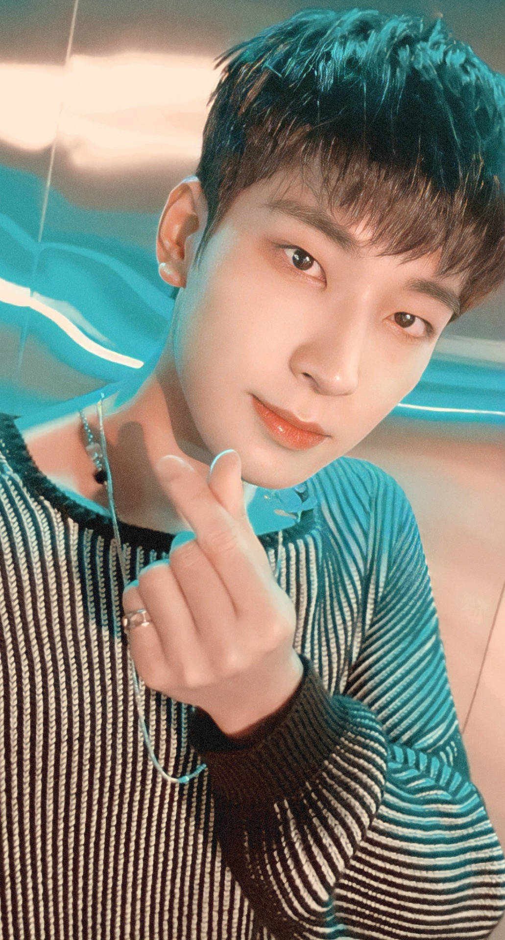 Wonwoo 桌布 壁紙 — 一位擁有青綠色頭髮和條紋毛衣的年輕男子，在發光的藍色背景前做出手指愛心手勢。