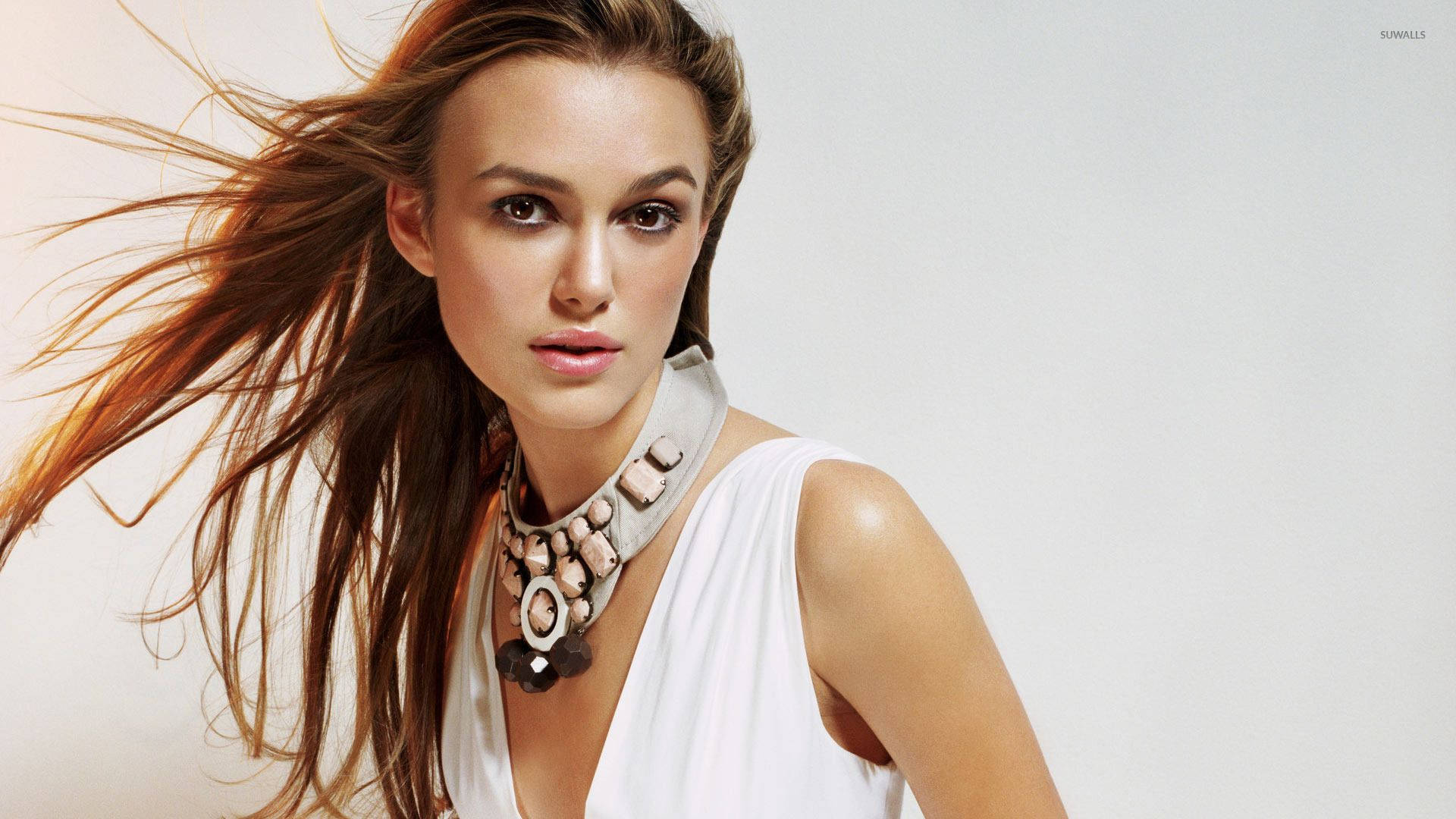 Keira Knightley 桌布 壁紙 — 一位擁有飄逸棕色頭髮和個性項鍊的女性，在純白色背景前直視鏡頭。