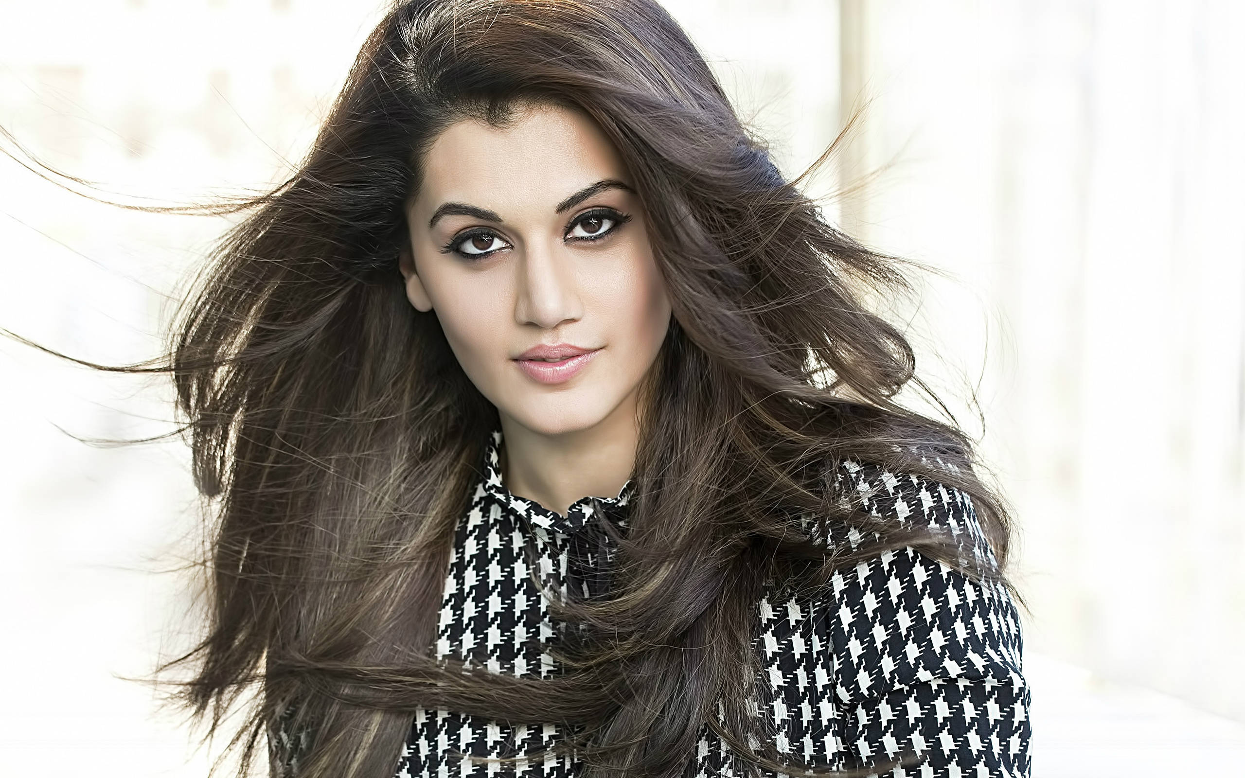 Taapsee Pannu 桌布 壁紙 — 一位擁有飄逸深色長髮和大膽妝容的女性，自信地凝視著，身穿黑白千鳥格上衣。