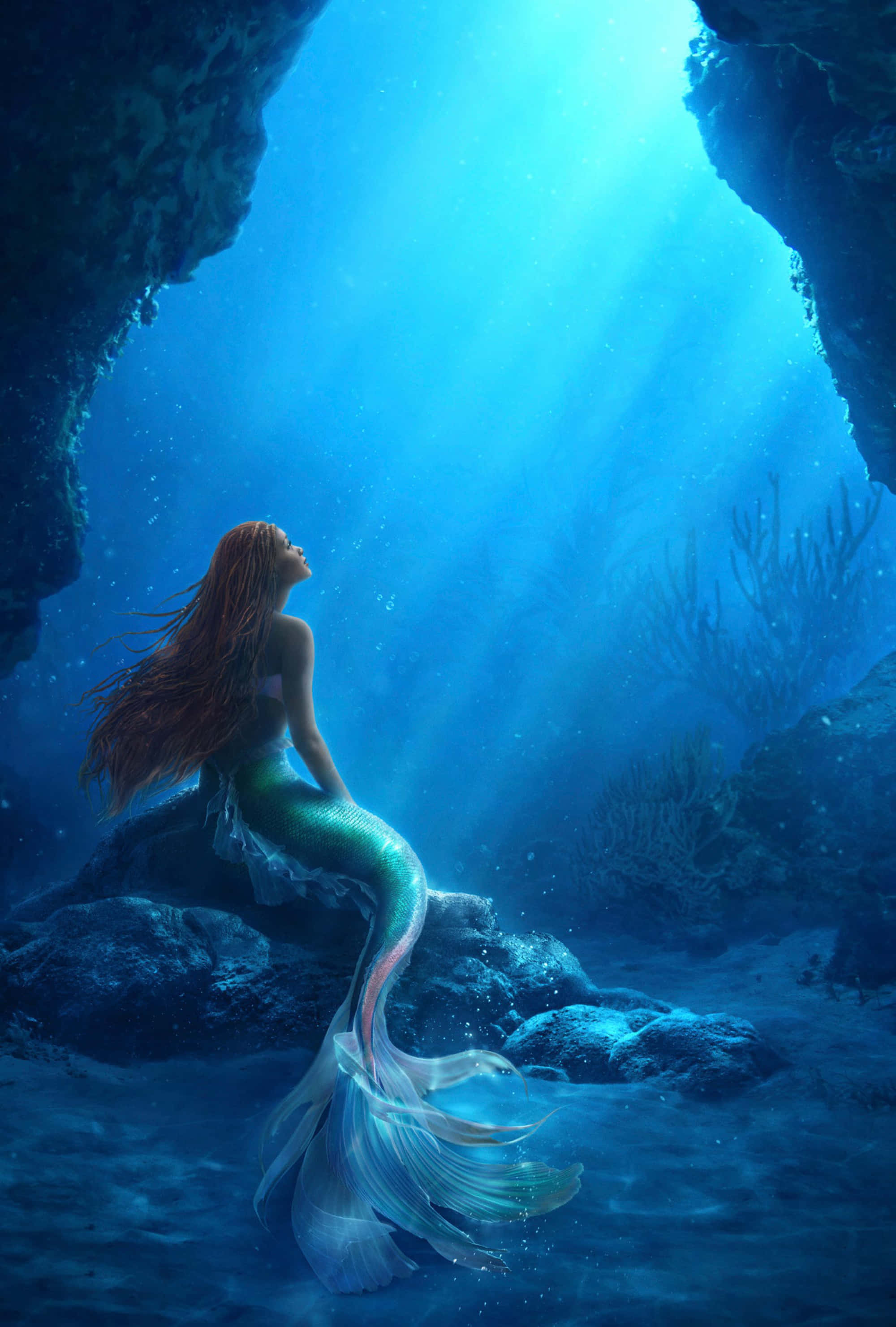 The Little Mermaid 桌布 壁紙 — 一位擁有飄逸紅髮的美人魚優雅地坐在陽光照射的水下洞穴中的岩石上，她閃爍著虹彩的尾巴在光線穿透深藍色海水時閃閃發光。
