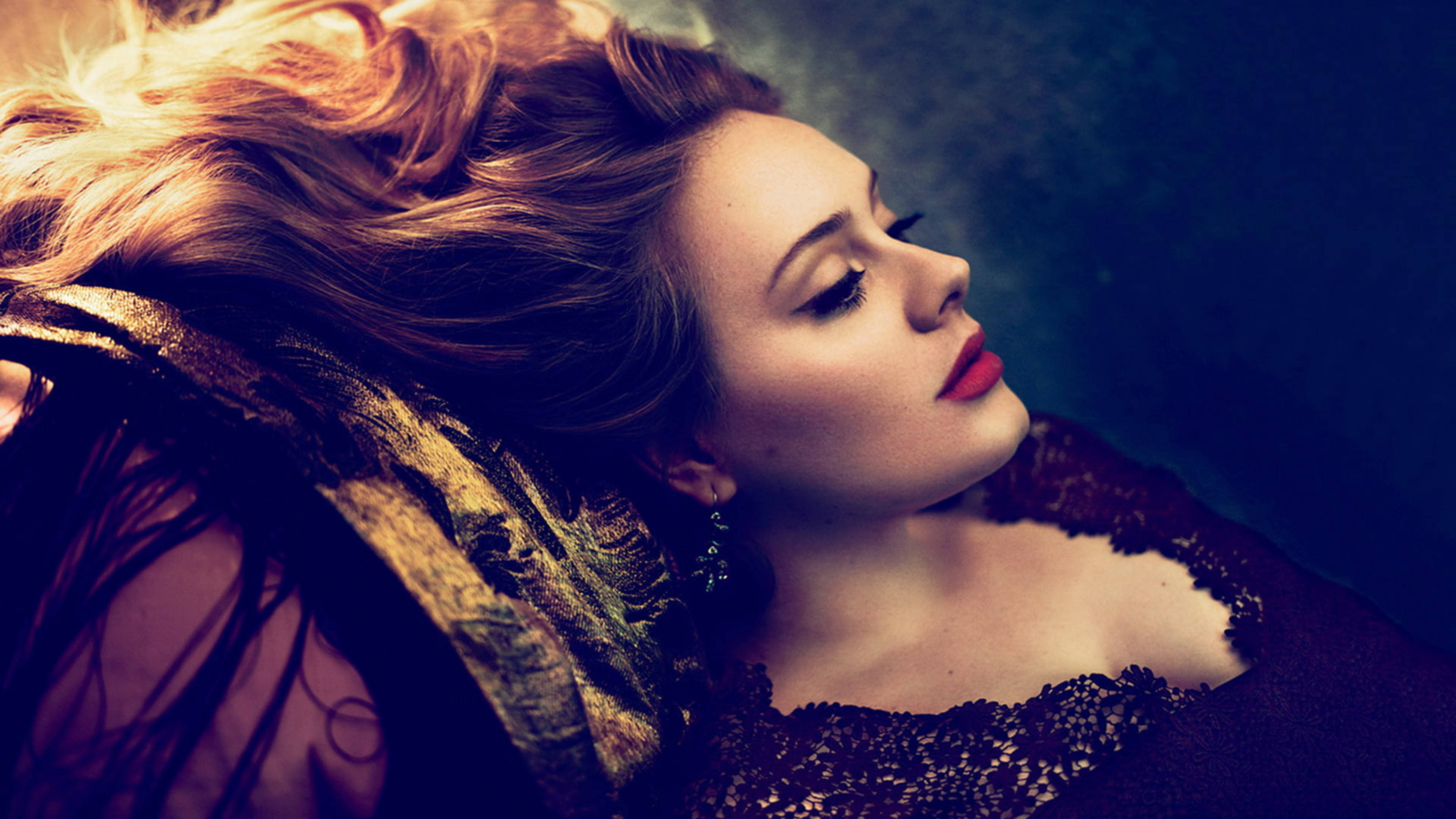 Adele 桌布 壁紙 — 一位擁有飄逸金髮和紅唇的女性，在陰暗憂鬱的背景下，披著華麗布料，頭部休息。