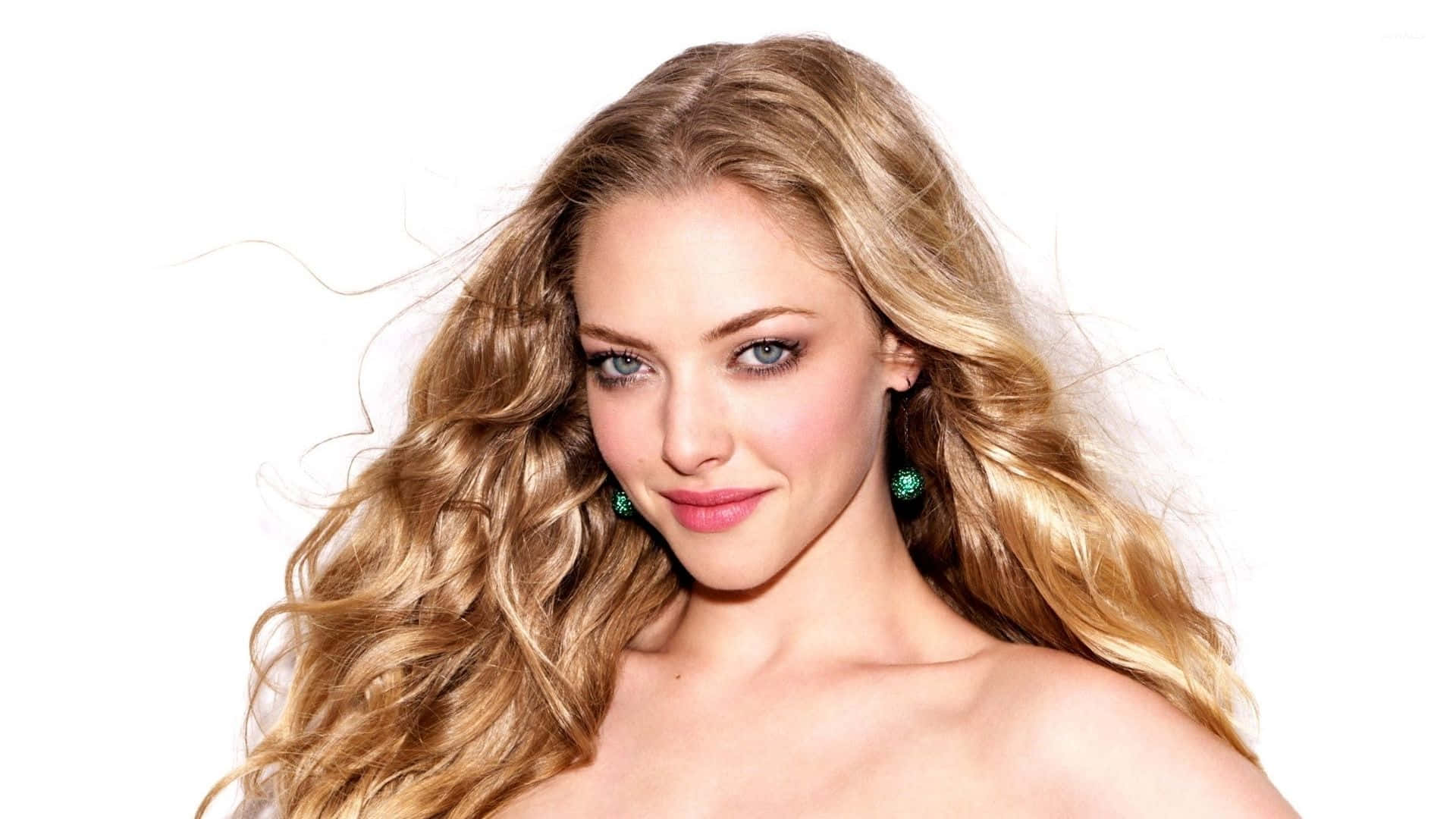 Amanda Seyfried 桌布 壁紙 — 一位擁有飄逸金髮和藍色眼睛的女性，在純白背景前溫柔微笑。