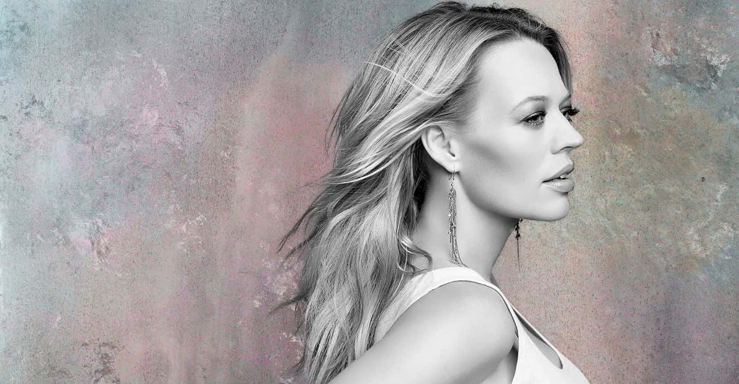 Jeri Ryan 桌布 壁紙 — 一位擁有飄逸金髮的女性，在紋理粉彩背景前若有所思地凝視。
