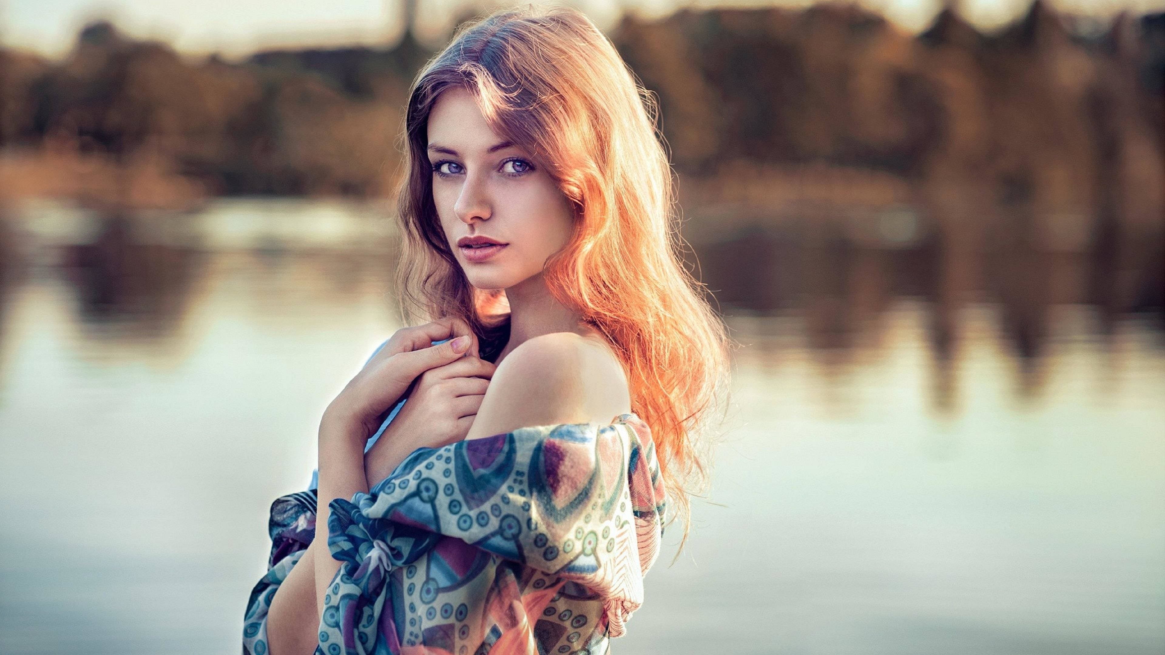 Beautiful Woman 桌布 壁紙 — 一位擁有飄逸金髮的女性站在寧靜的湖邊，穿著色彩繽紛的圖案露肩上衣，金色光芒沐浴著她。