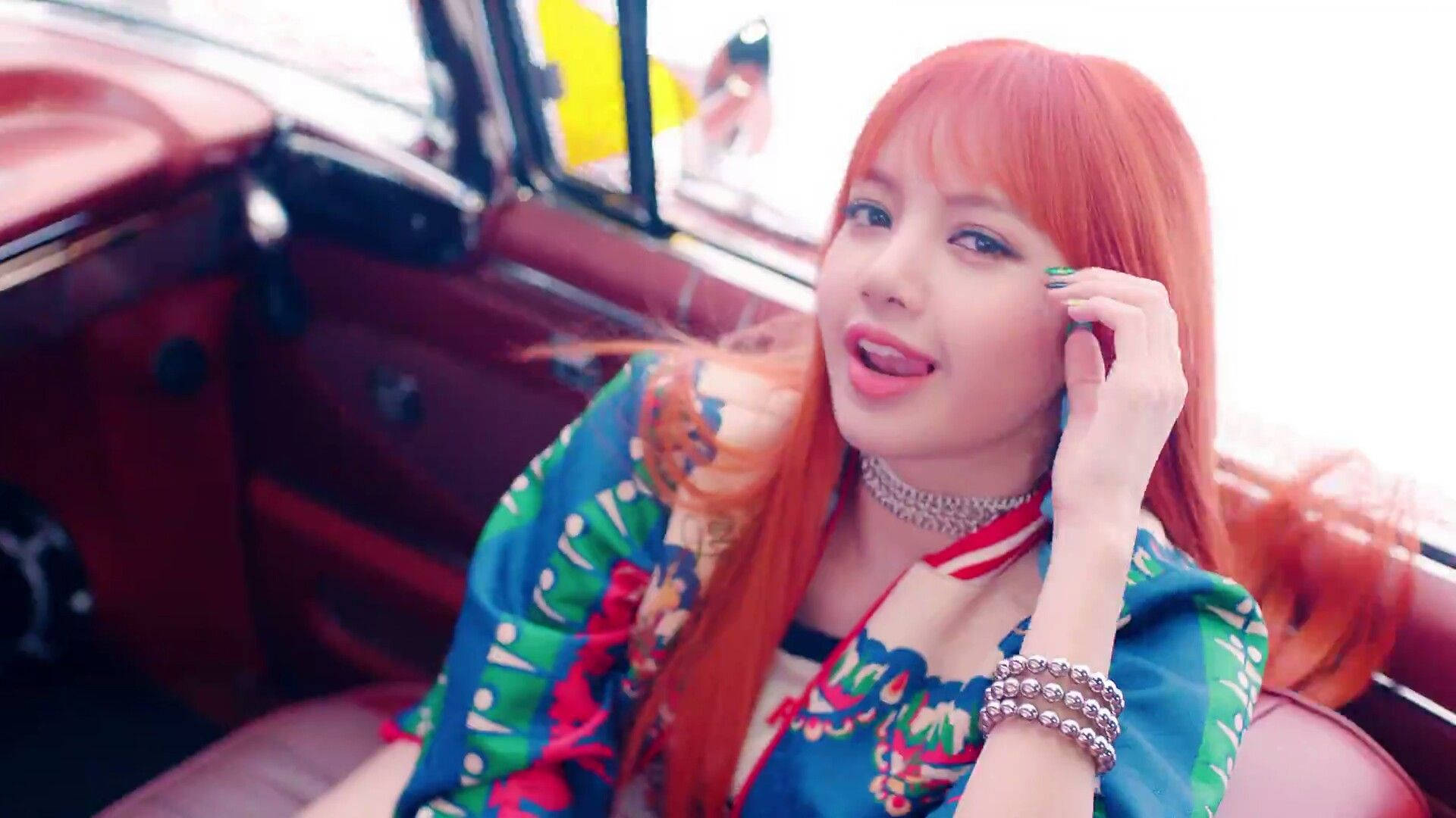 Lalisa 桌布 壁紙 — 一位擁有鮮豔橙色頭髮的女性坐在一輛紅色復古車中，穿著色彩繽紛的花卉上衣和銀飾，看起來很調皮。
