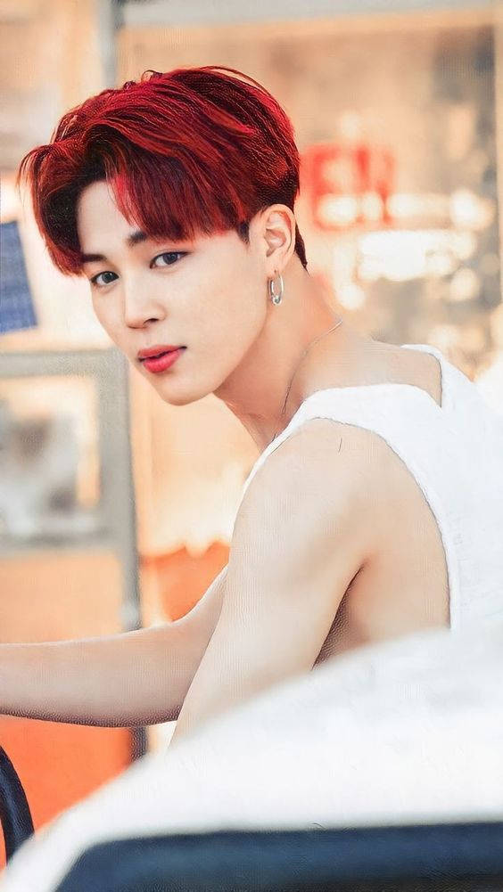 BTS 智旻 桌布 壁紙 — 一位擁有鮮豔紅髮、身穿白色背心的年輕男子，在溫暖燈光的室內環境中回頭凝視。