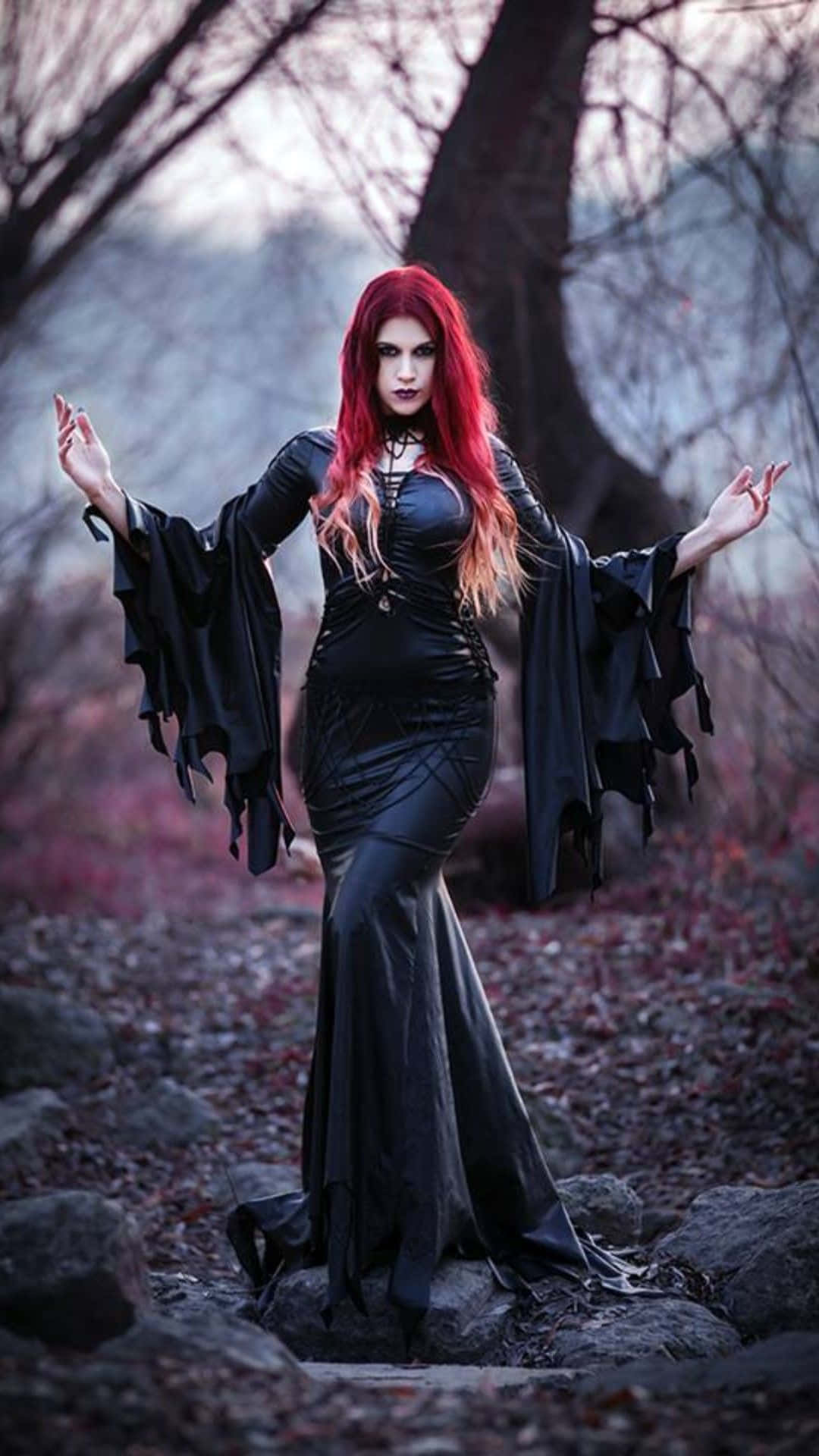 Dark Witch 桌布 壁紙 — 一位擁有鮮豔紅髮、身穿黑色哥德式長袍的女性，戲劇性地站在一片薄霧籠罩、樹木光禿、落葉滿地的森林中。
