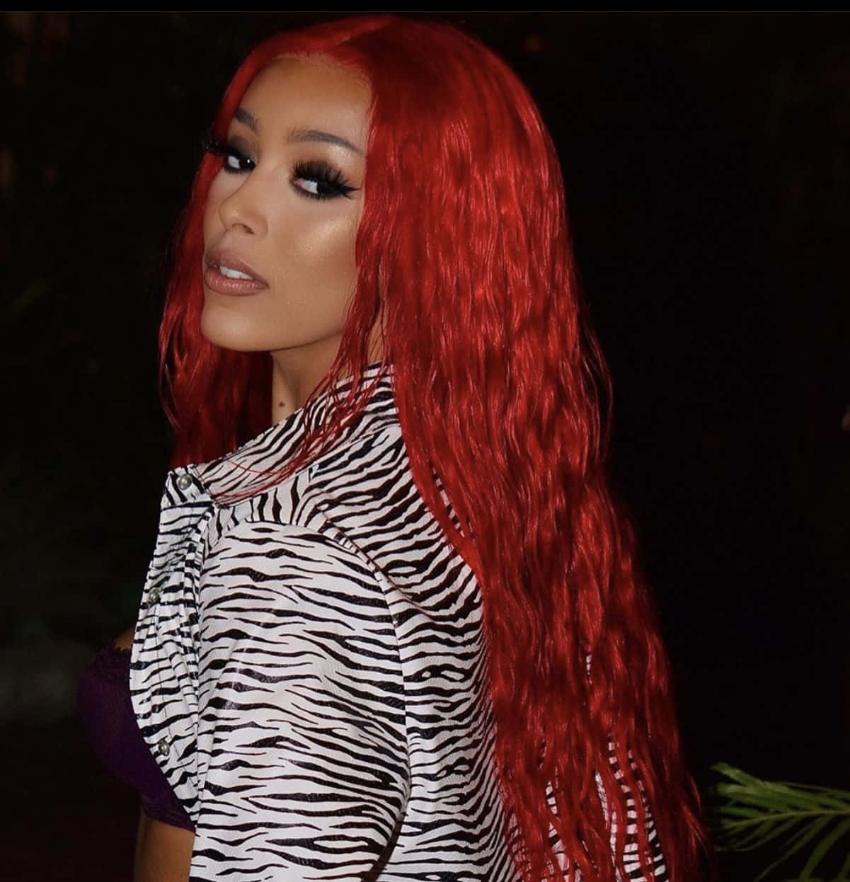 Doja Cat 桌布 壁紙 — 一位擁有鮮豔紅髮和大膽妝容的女性，在深色背景前穿著斑馬紋上衣。