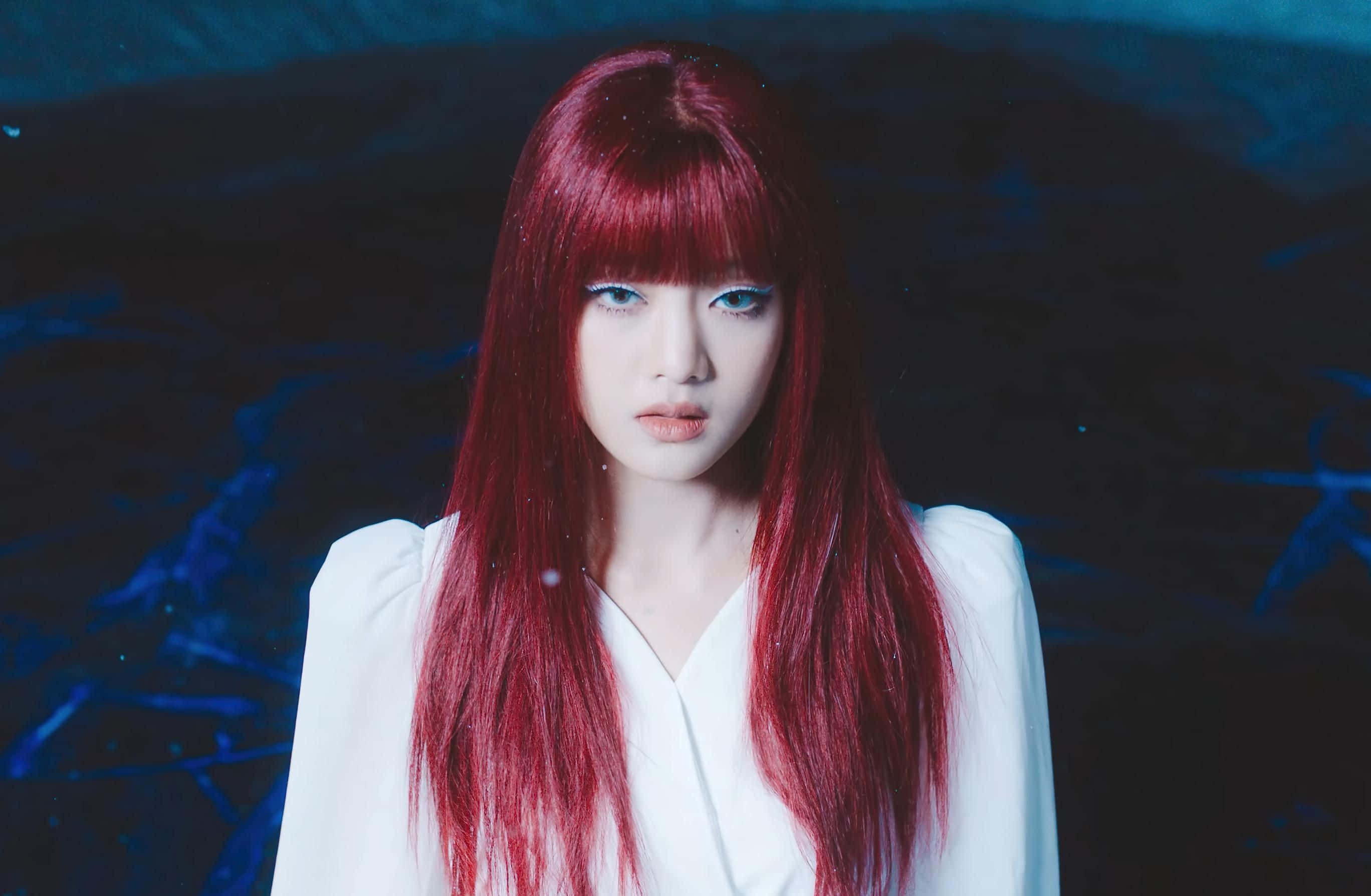K-pop 桌布 壁紙 — 一位擁有鮮豔紅髮和引人注目的藍眼睛的女性，身穿白色襯衫，在深藍色紋理背景前直視前方。