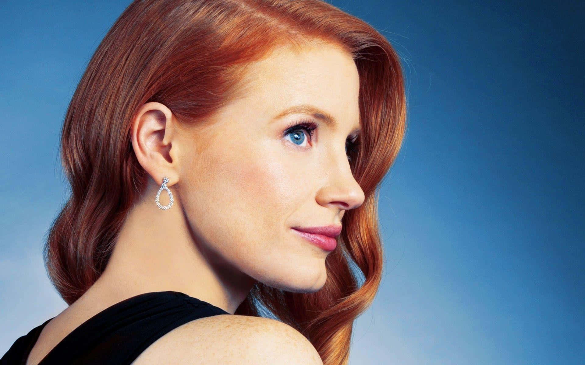 jessica chastain 桌布 壁紙 — 一位擁有鮮豔紅髮和引人注目的藍眼睛的女性，在柔和的藍色漸變背景前若有所思地凝視。
