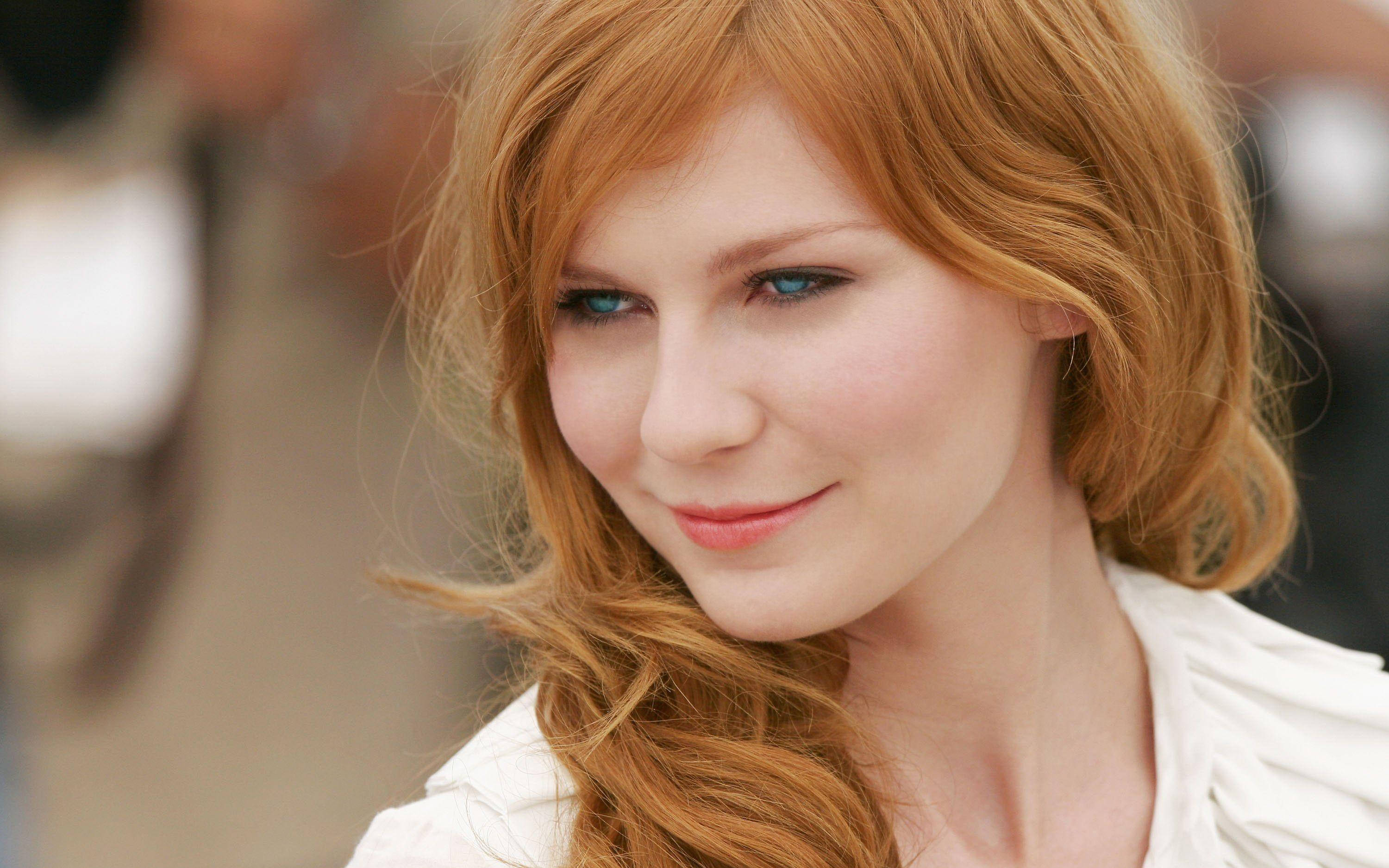 Kirsten Dunst 桌布 壁紙 — 一位擁有鮮豔紅髮和引人注目的藍眼睛的女性微笑的特寫肖像。