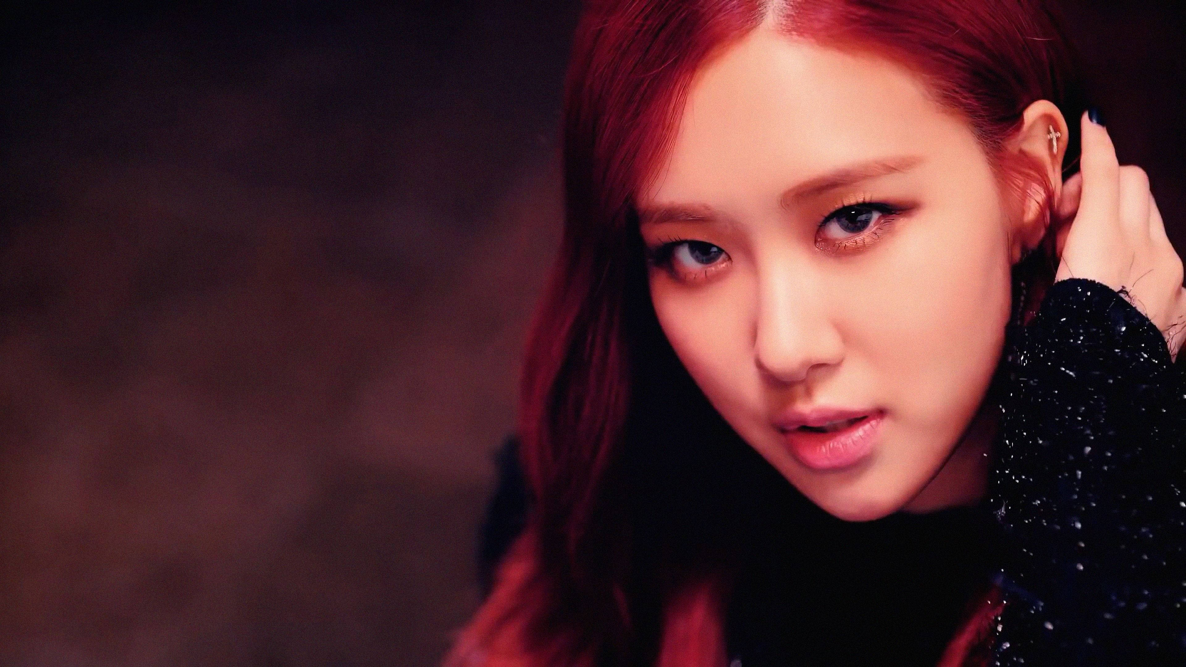BLACKPINK 桌布 壁紙 — 一位擁有鮮豔紅髮和強烈眼神的女性的特寫肖像，穿著黑色閃亮上衣，背景陰暗有氣氛。