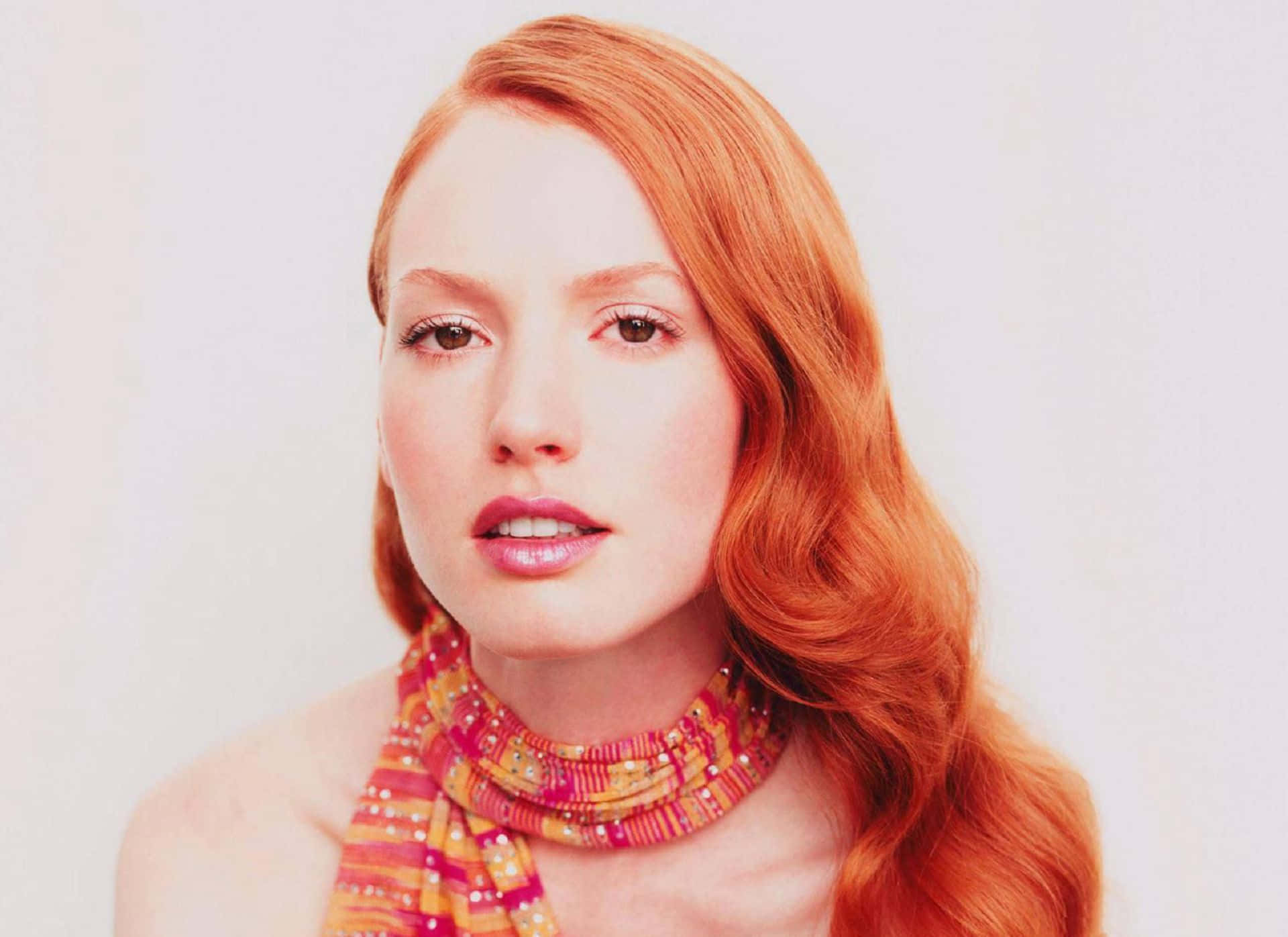 Alicia Witt 桌布 壁紙 — 一位擁有鮮豔紅髮和彩色珠飾圍巾的女性，在純白背景前溫柔凝視。