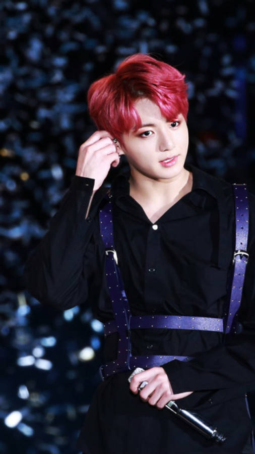 Jungkook 桌布 壁紙 — 一位擁有鮮豔紅髮和黑色服裝的表演者，在閃爍的藍色背景下手持麥克風。