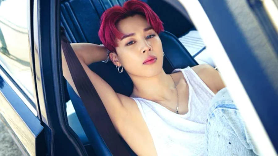BTS 智旻 桌布 壁紙 — 一位擁有鮮豔紅髮的人，穿著白色背心和牛仔褲，隨意地靠在汽車座椅上。