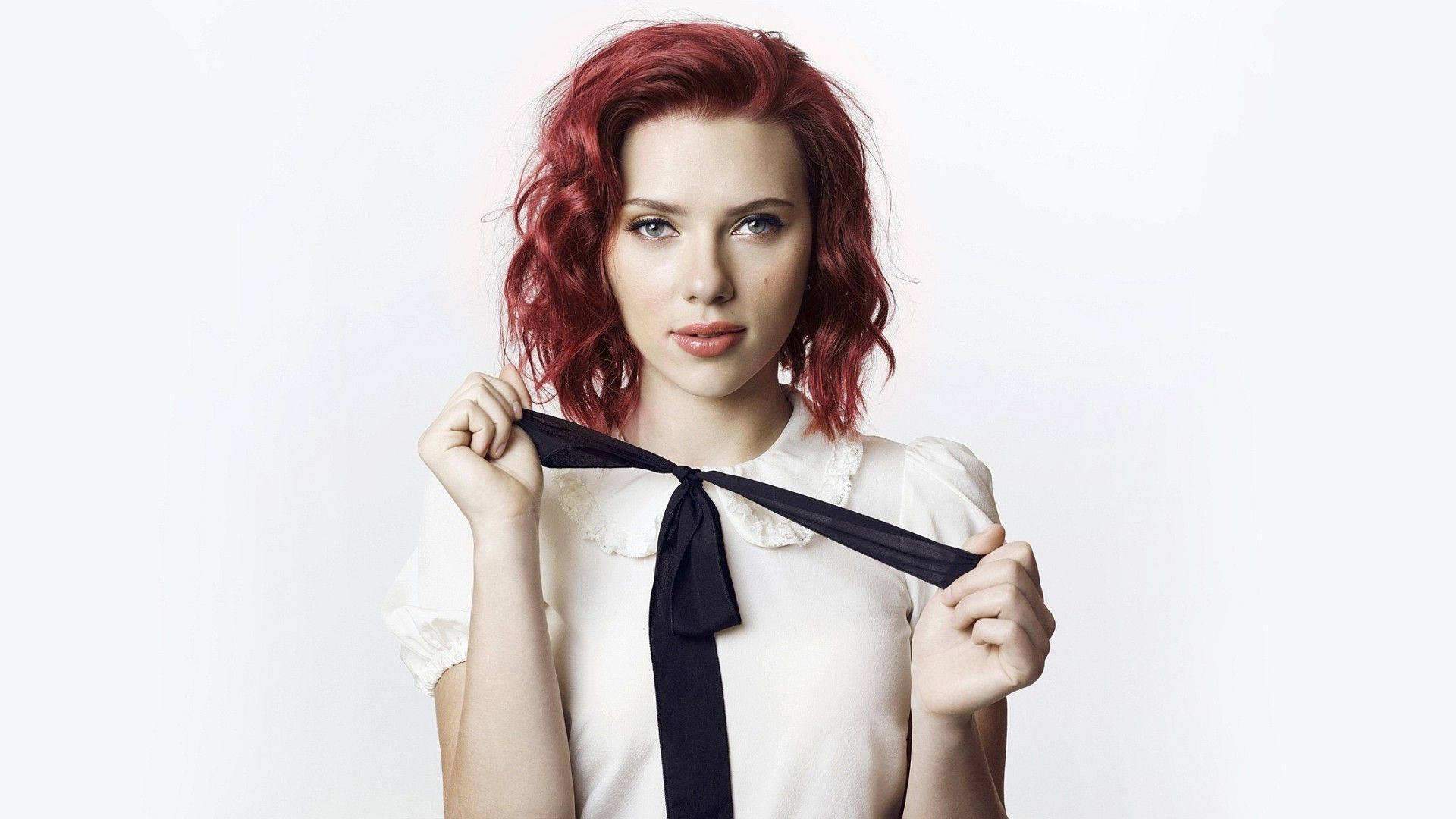 Scarlett 桌布 壁紙 — 一位擁有鮮豔紅髮的女性，在純白背景前手持黑色絲帶，眼神直接而強烈。