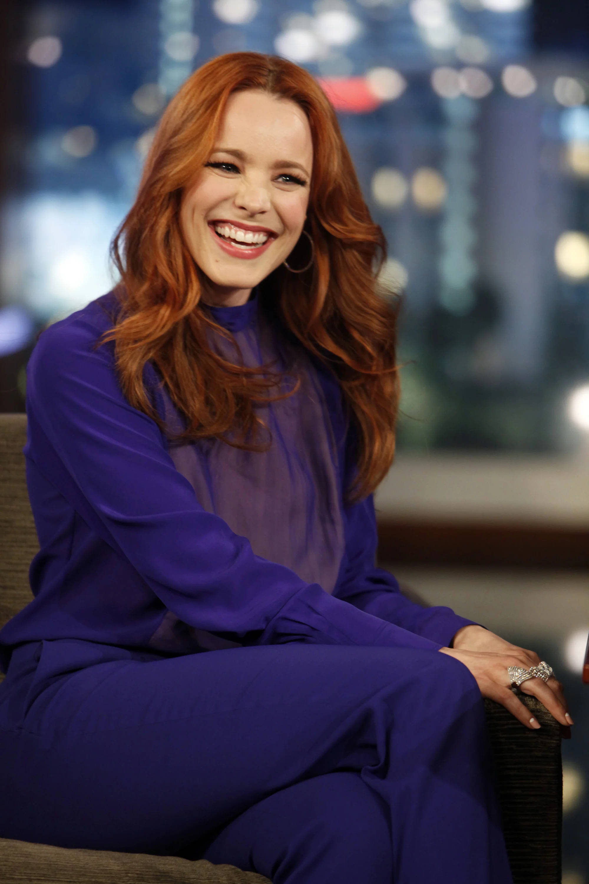 Rachel Mcadams 桌布 壁紙 — 一位擁有鮮豔紅髮的女性，身穿皇家藍色服裝，在模糊的城市景觀背景下閃耀。