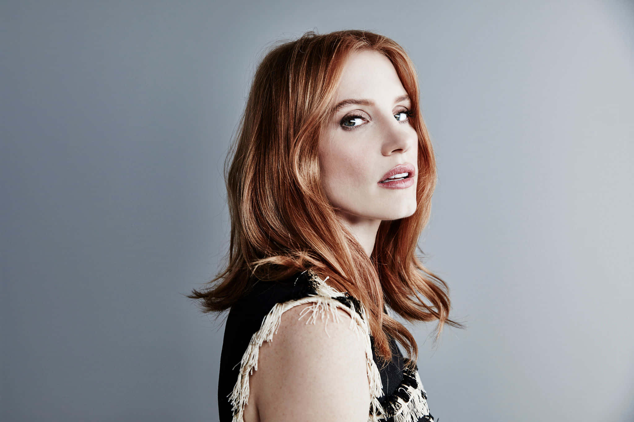 jessica chastain 桌布 壁紙 — 一位擁有鮮豔紅髮的女性在柔和的灰色工作室背景下若有所思地凝視。