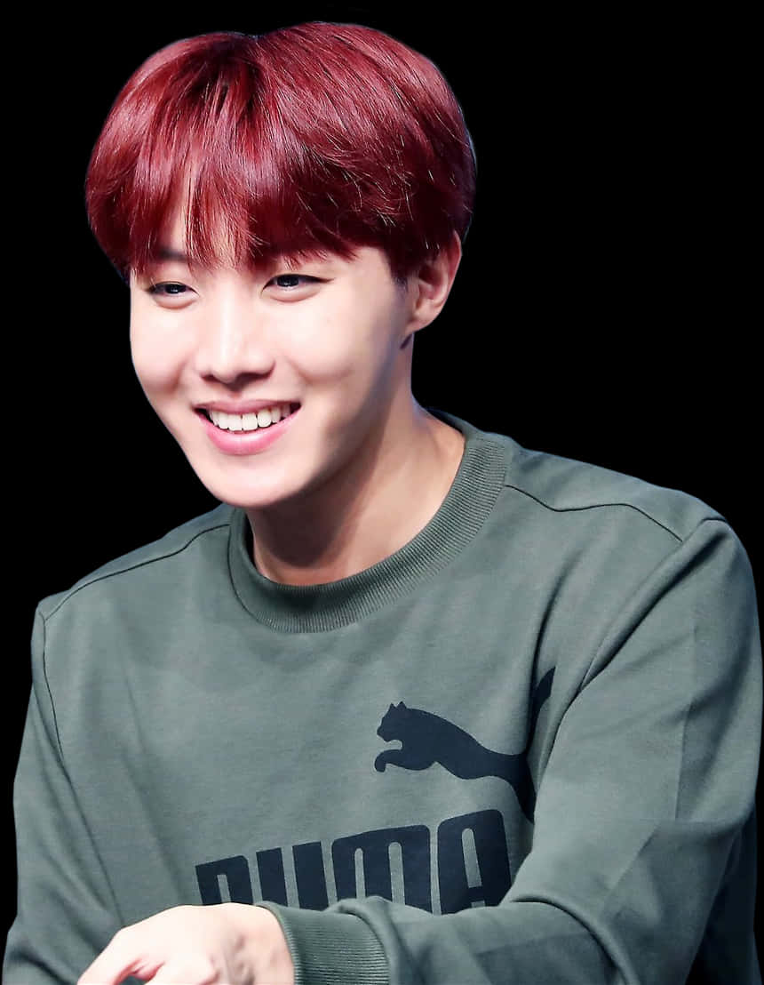 BTS 桌布 壁紙 — 一位擁有鮮豔紅髮的年輕男子，在黑色背景前穿著綠色Puma運動衫，溫暖地微笑。