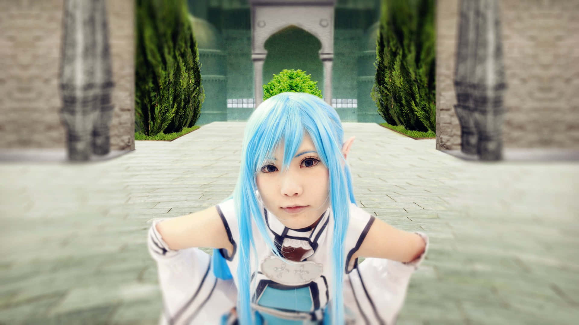 Sword Art Online Cosplay 桌布 壁紙 — 一位擁有鮮豔藍色頭髮和精靈耳朵的角色扮演者，身穿白色服裝，在兩旁高聳綠色樹籬的石拱門前擺姿勢。