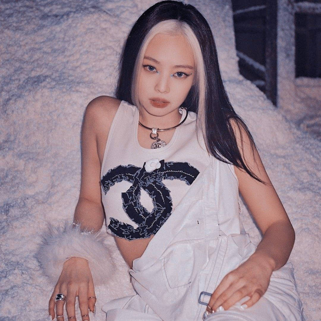 珍妮·金 桌布 壁紙 — 一位擁有黑白頭髮的女性，穿著白色 Chanel 套裝，自信地坐在有紋理的灰色背景前。