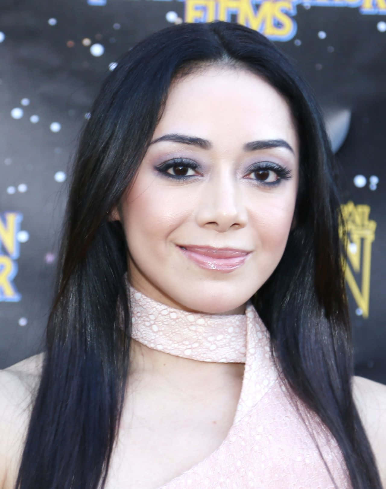 Aimee Garcia 桌布 壁紙 — 一位擁有黑色長髮、身穿粉紅色連衣裙的女性，在星光熠熠的活動背景下對著鏡頭微笑。