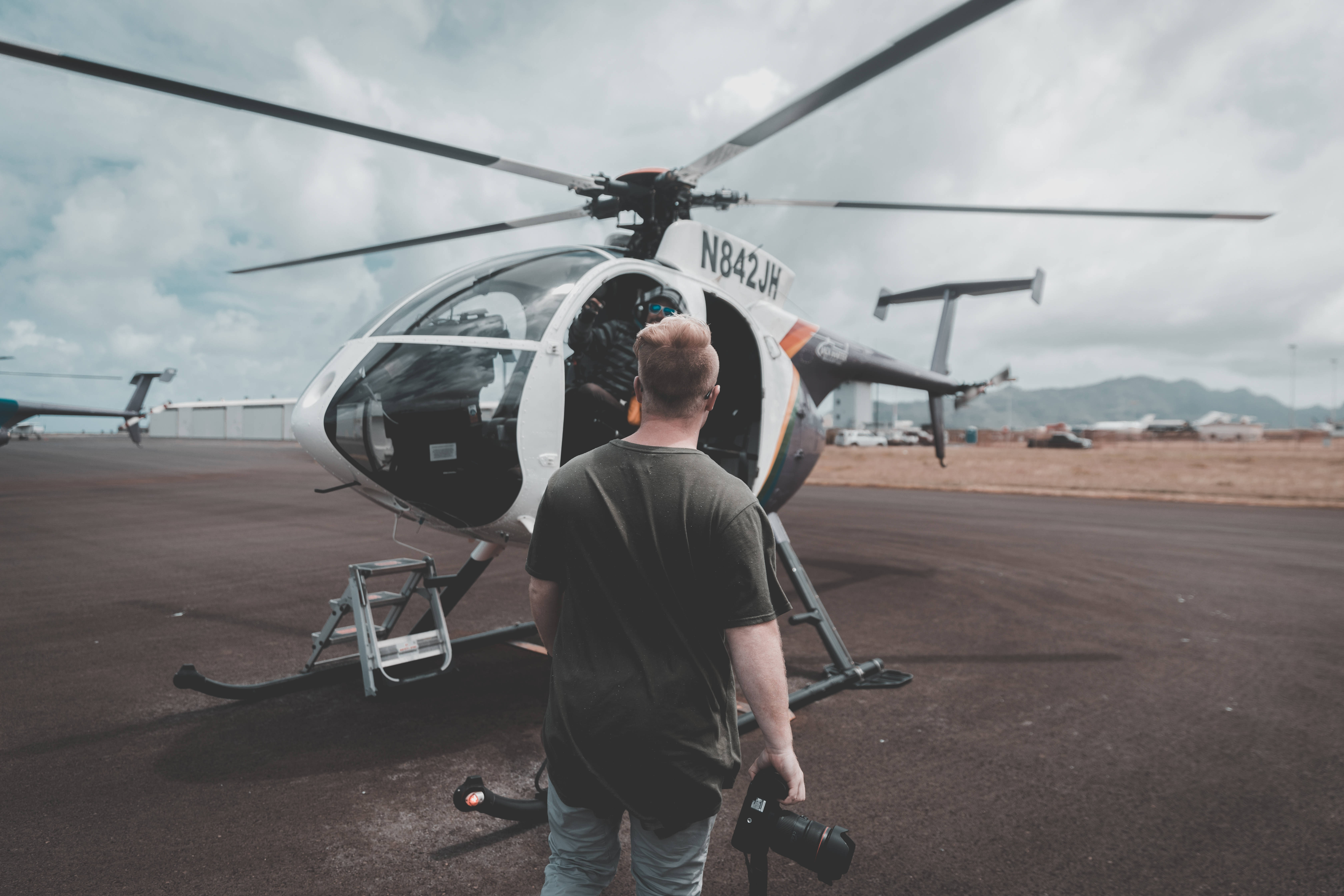 Helicopter 桌布 壁紙 — 一位攝影師拿著相機，在陰天停機坪上走近一架白色直升機。
