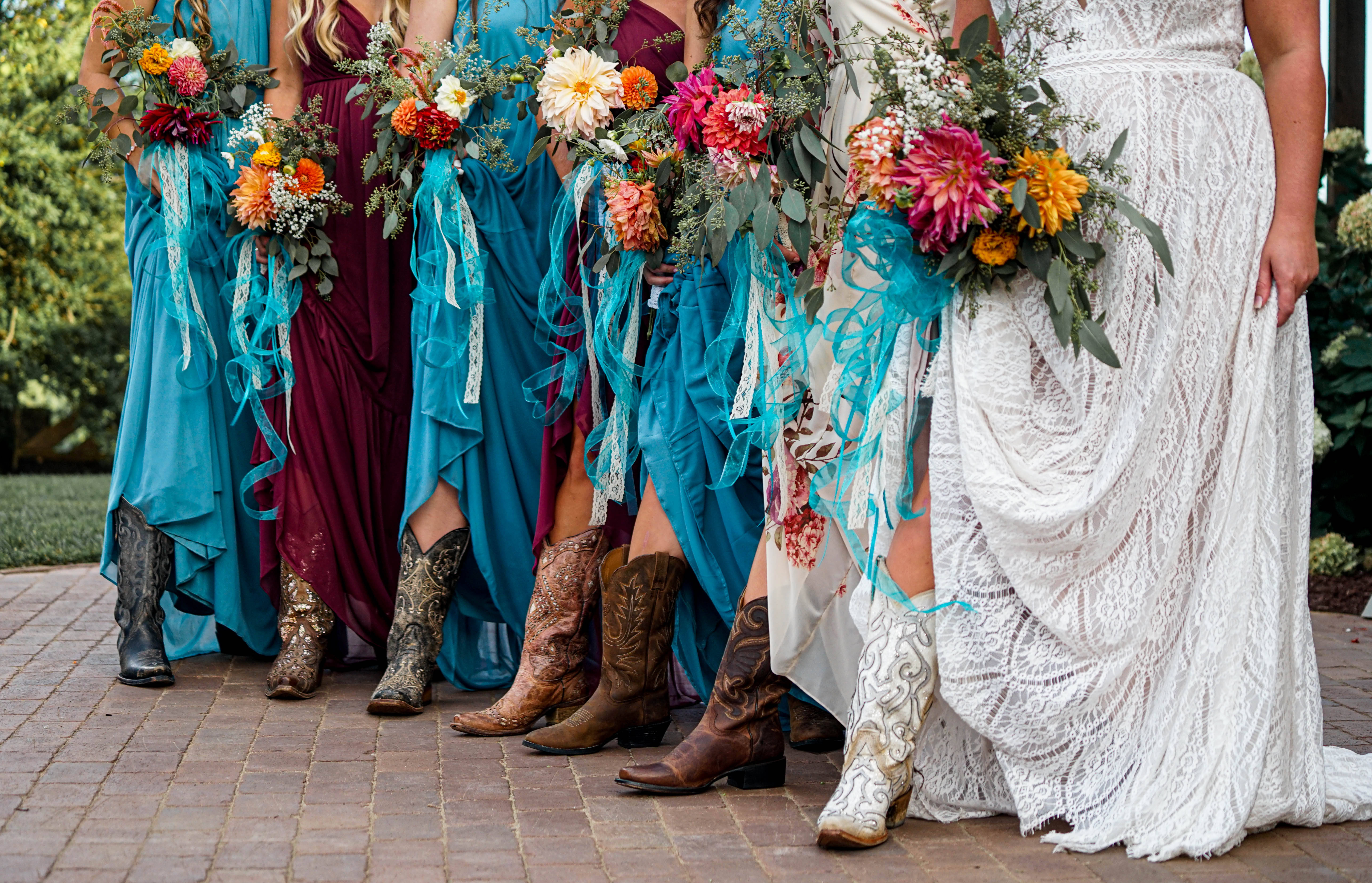 Bridesmaids 桌布 壁紙 — 一位新娘和伴娘穿著飄逸的連衣裙和牛仔靴，在磚砌庭院中手持鮮豔的花束。