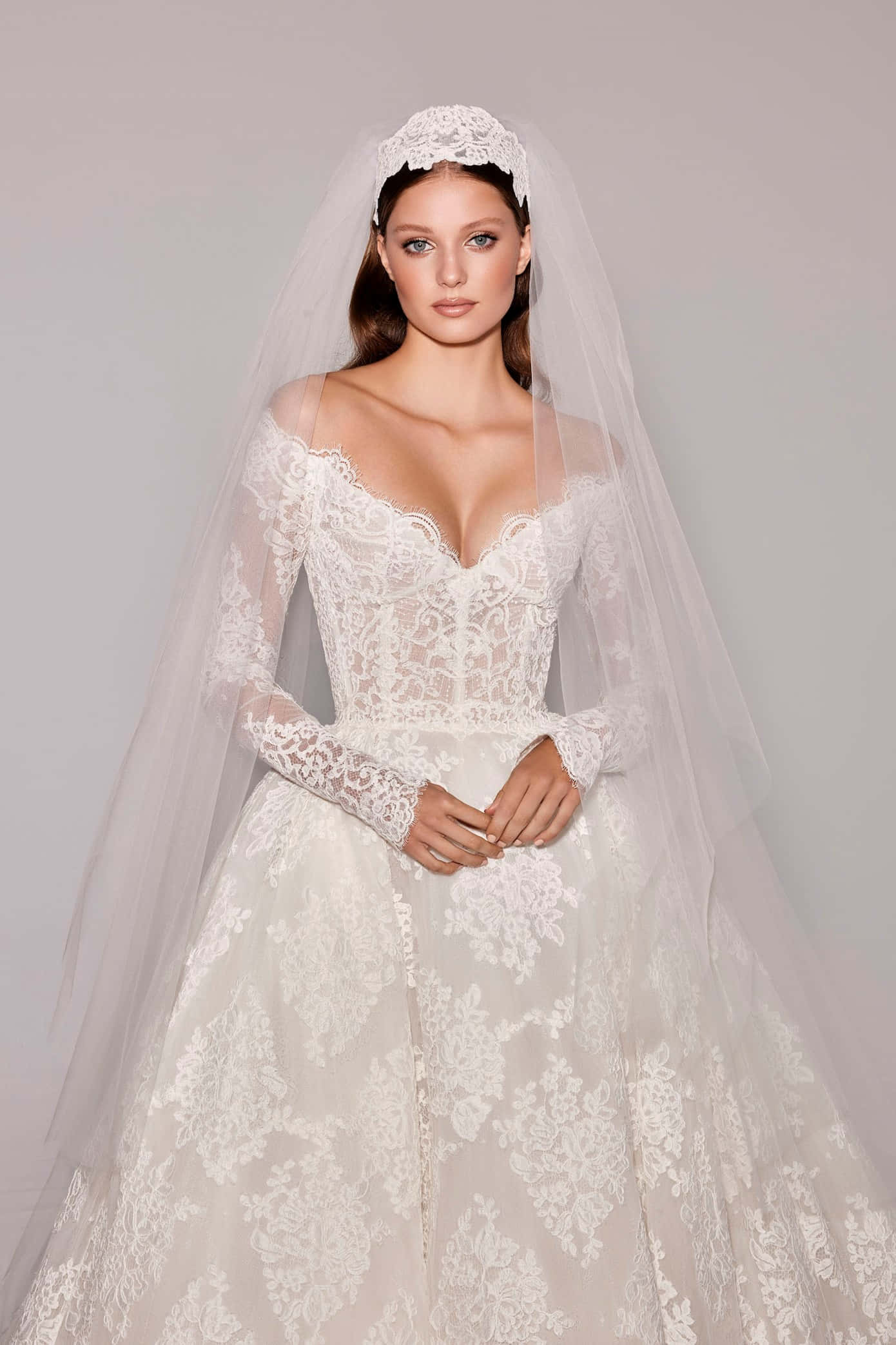 Bride's Dress 桌布 壁紙 — 一位新娘穿著優雅的白色蕾絲婚紗，長袖和飄逸的頭紗，在柔和的灰色背景前擺姿勢。