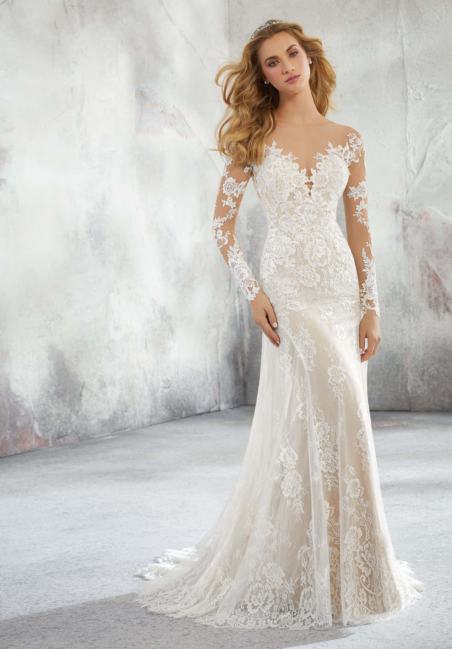 Wedding Gown 桌布 壁紙 — 一位新娘穿著優雅的白色蕾絲美人魚婚紗，長袖和深領口，在帶紋理的灰色背景前優雅地擺姿勢。