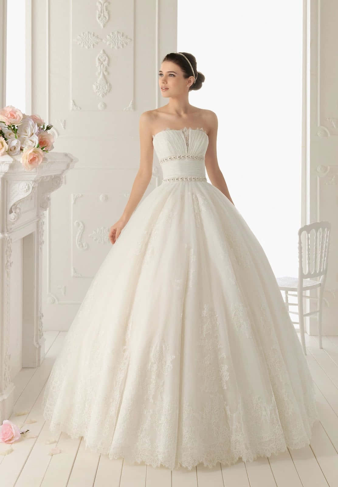 Wedding Gown 桌布 壁紙 — 一位新娘穿著寬大的白色蕾絲婚紗，優雅地站在一個明亮華麗、帶有花卉裝飾的白色房間裡。