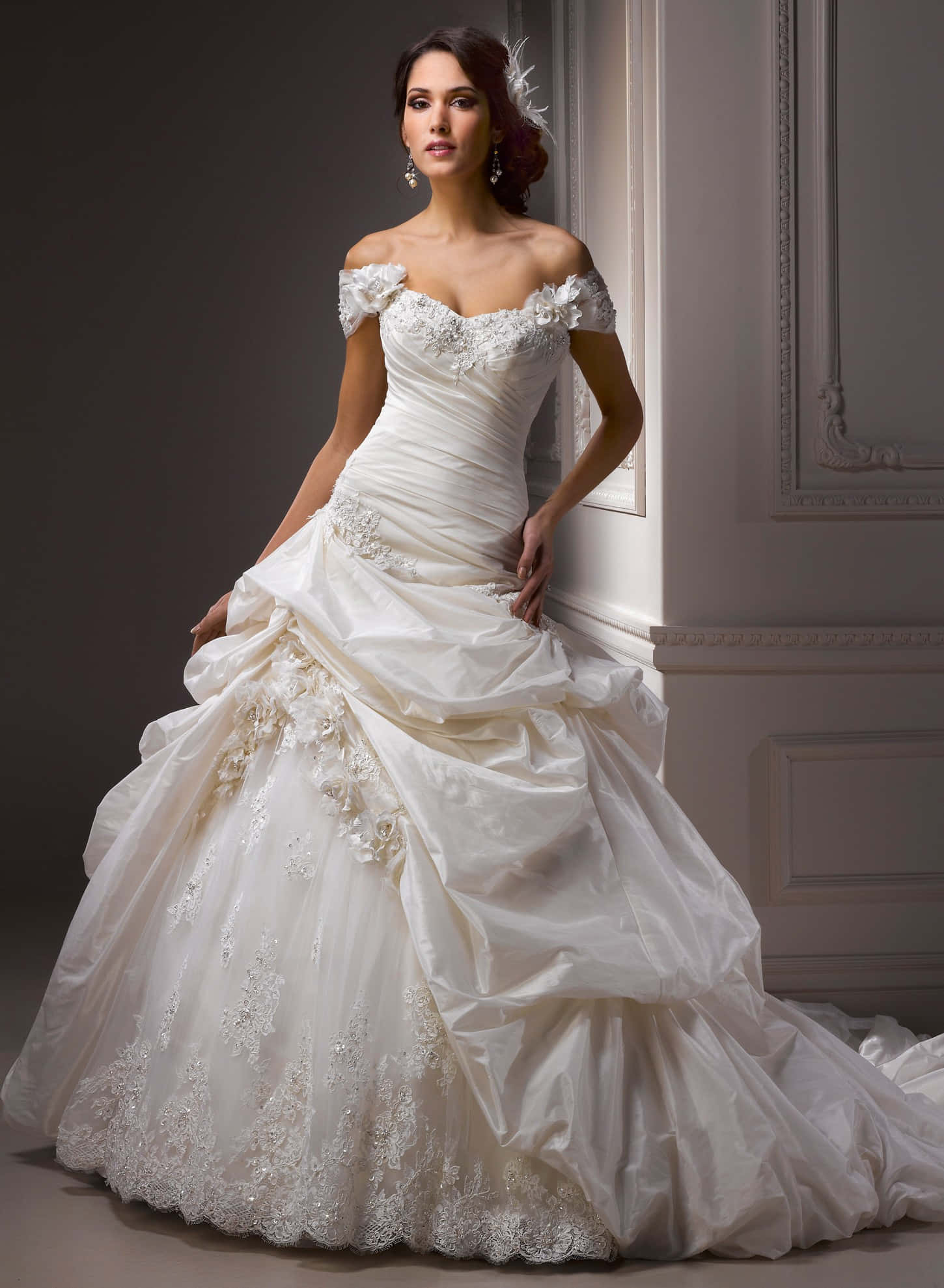 Wedding Gown 桌布 壁紙 — 一位新娘穿著露肩象牙色婚紗，飾有花卉蕾絲和荷葉邊，在經典的白色鑲板牆前優雅地擺姿勢。