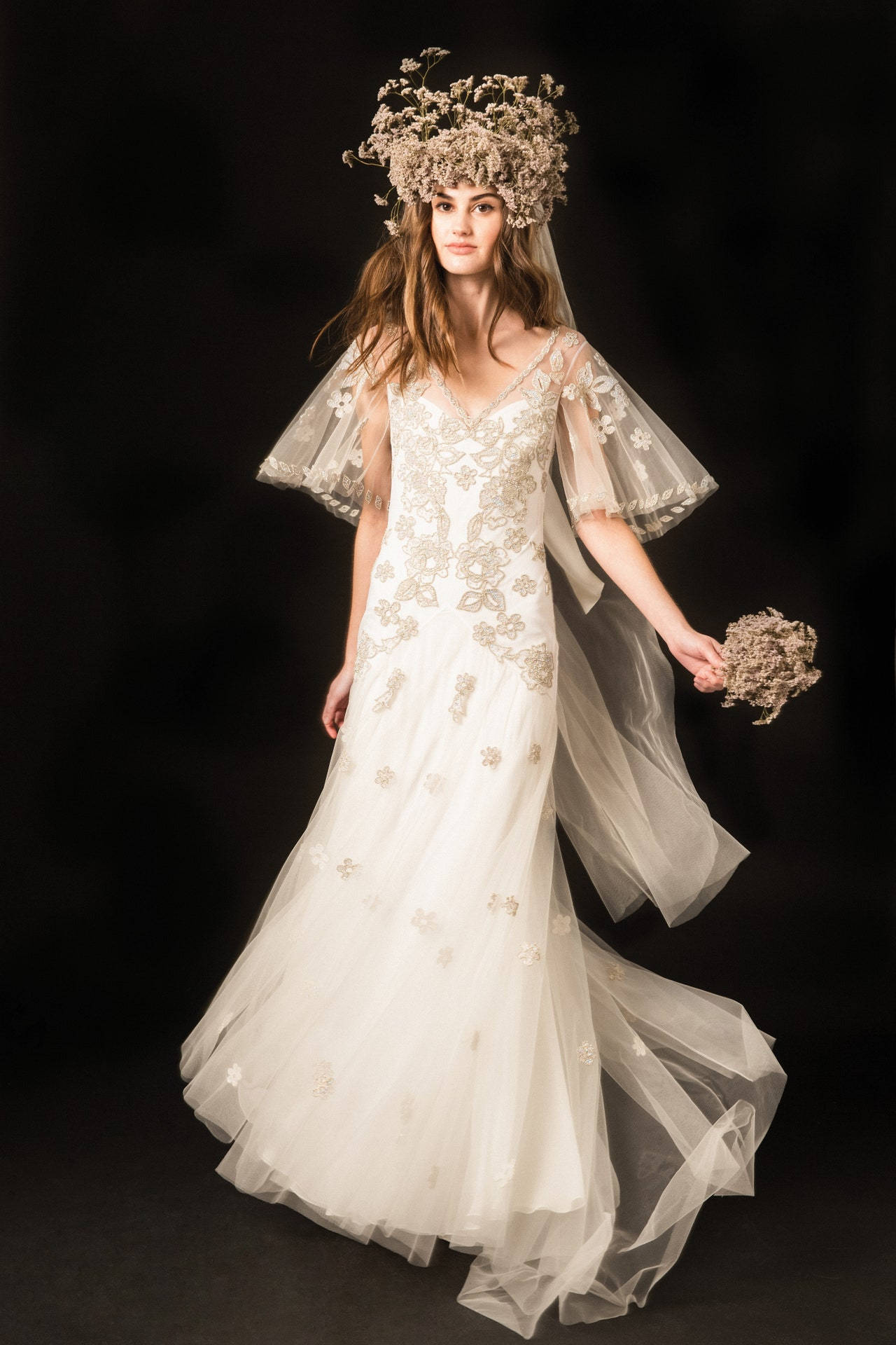 Bride 桌布 壁紙 — 一位新娘身穿飾有花卉刺繡的華麗白色禮服，搭配相襯的乾花花冠，在黑色背景前手持花束。