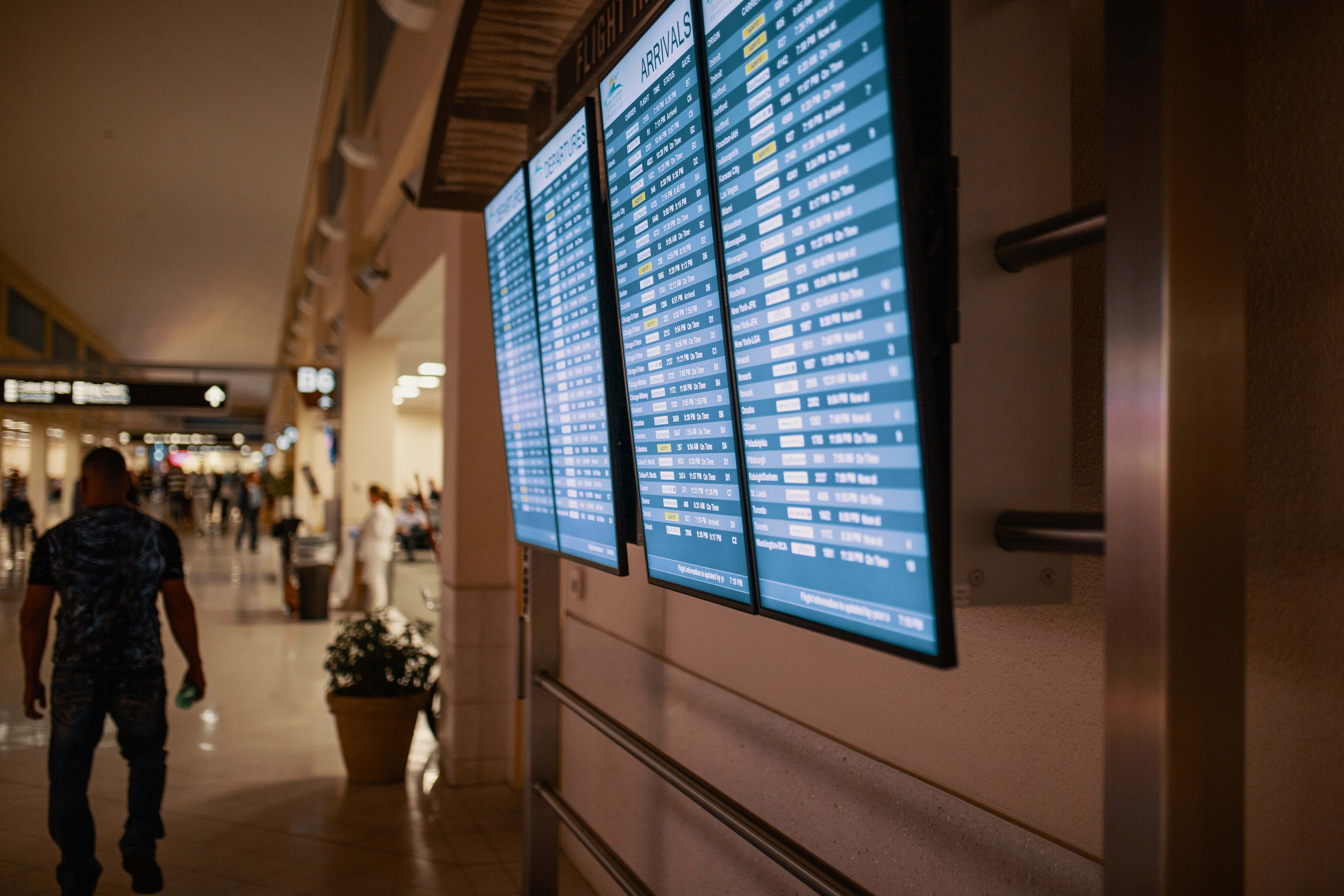 Airport 桌布 壁紙 — 一位旅客走過昏暗機場航廈走廊中發光的數位航班抵達顯示板。
