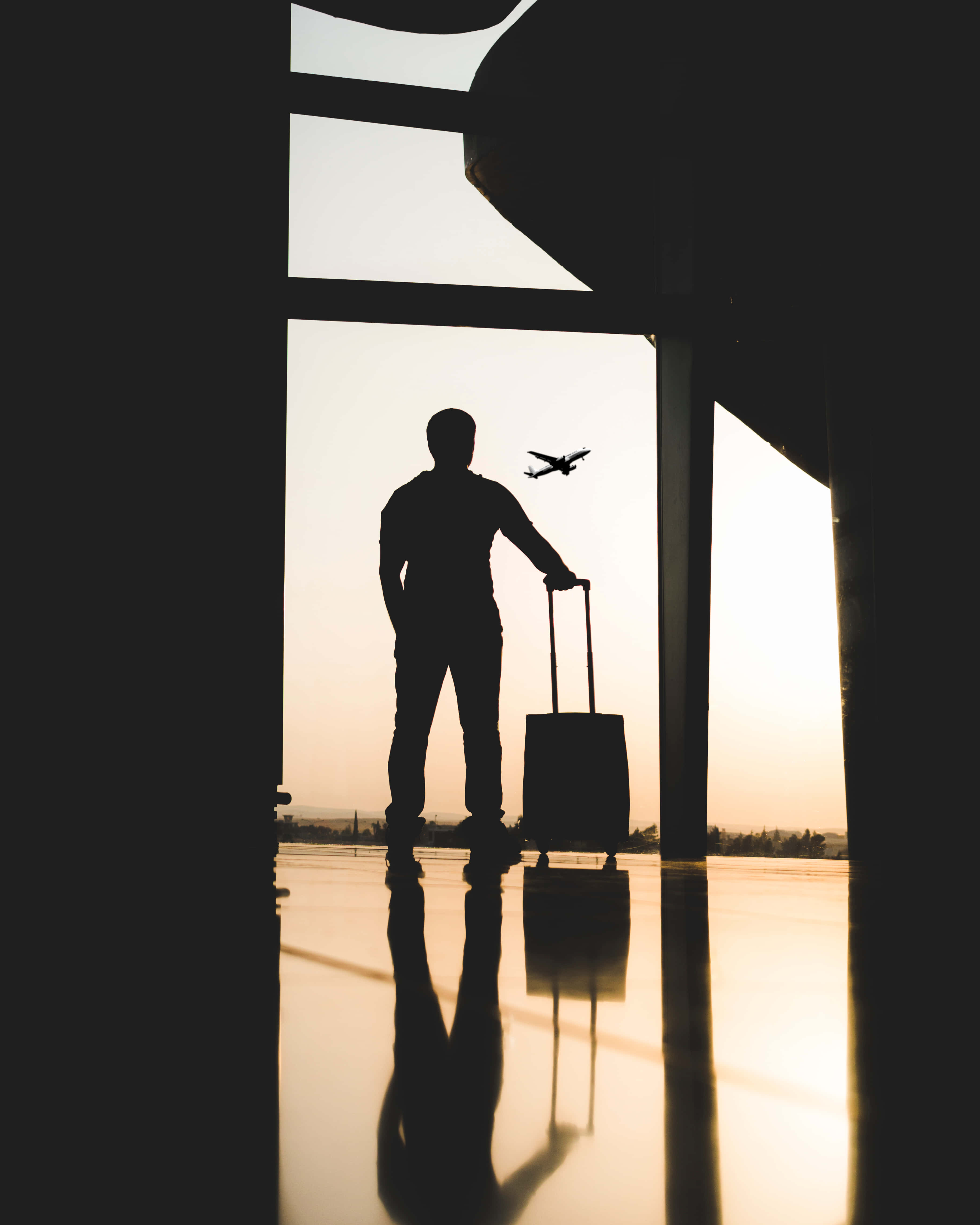 Silhouette 桌布 壁紙 — 一位旅行者拖著行李箱站在機場航廈的剪影，夕陽下一架飛機從頭頂飛過。