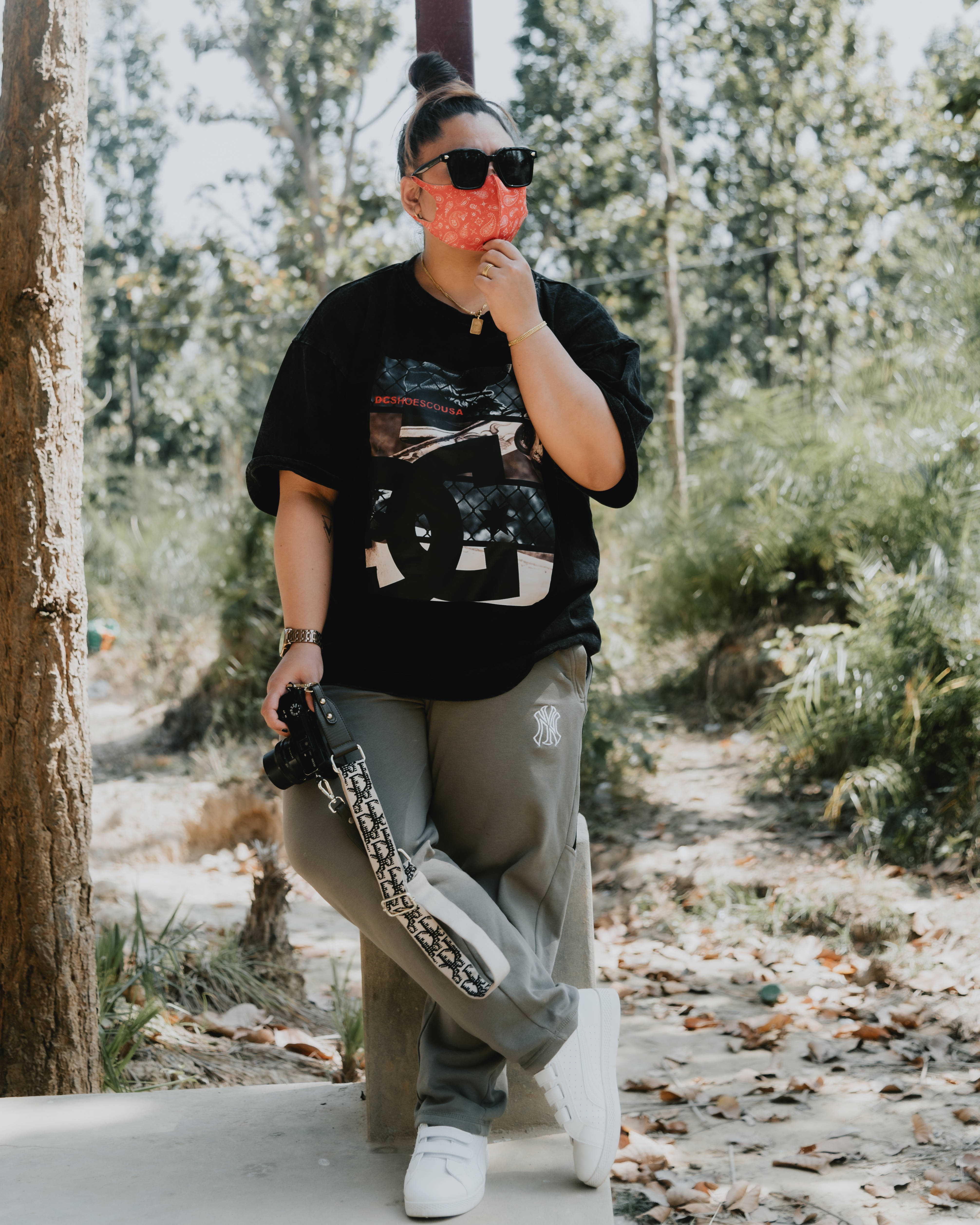 Tomboy 桌布 壁紙 — 一位時尚人士穿著黑色圖案T恤和灰色運動褲，在陽光明媚的森林中靠著一棵樹，戴著紅色圖案口罩和太陽眼鏡。