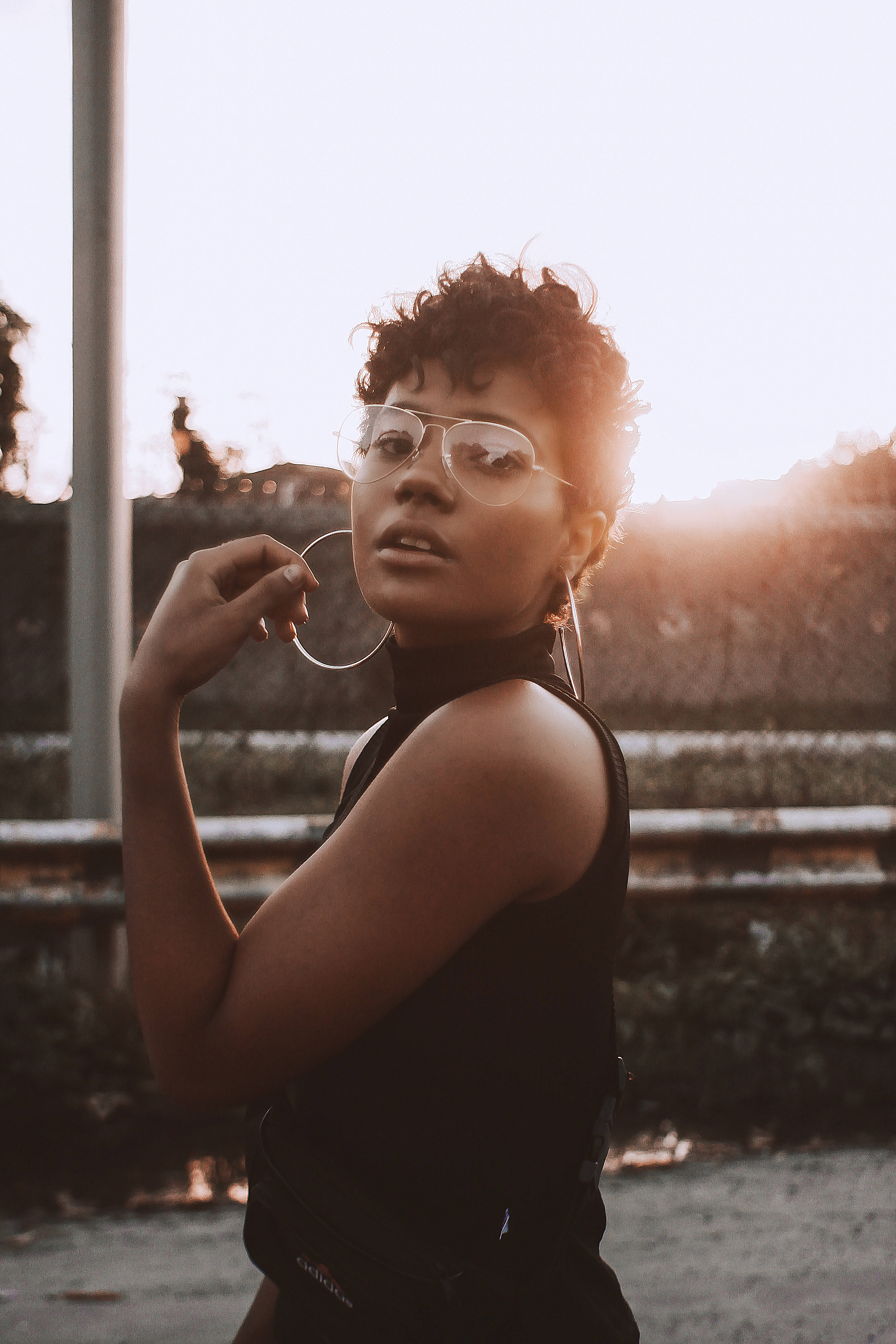 Black Girl 桌布 壁紙 — 一位時尚女性，擁有捲曲頭髮和大圈耳環，在陽光普照的城市背景下自信地擺姿勢。