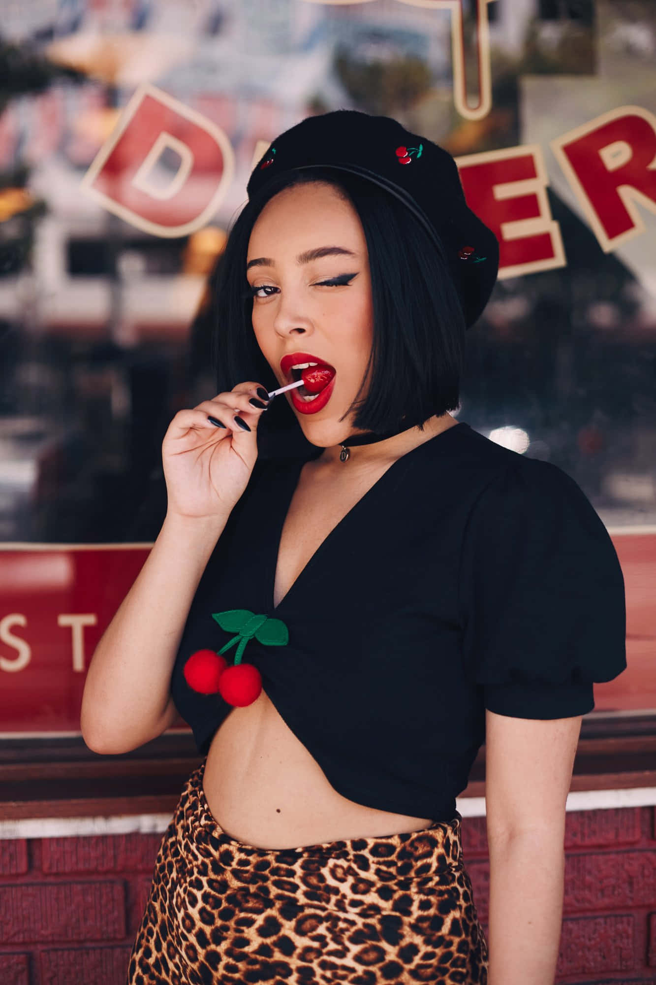 Doja Cat 桌布 壁紙 — 一位時尚女性，擁有鮮豔的紅唇和黑色貝雷帽，在復古餐廳招牌前塗口紅。
