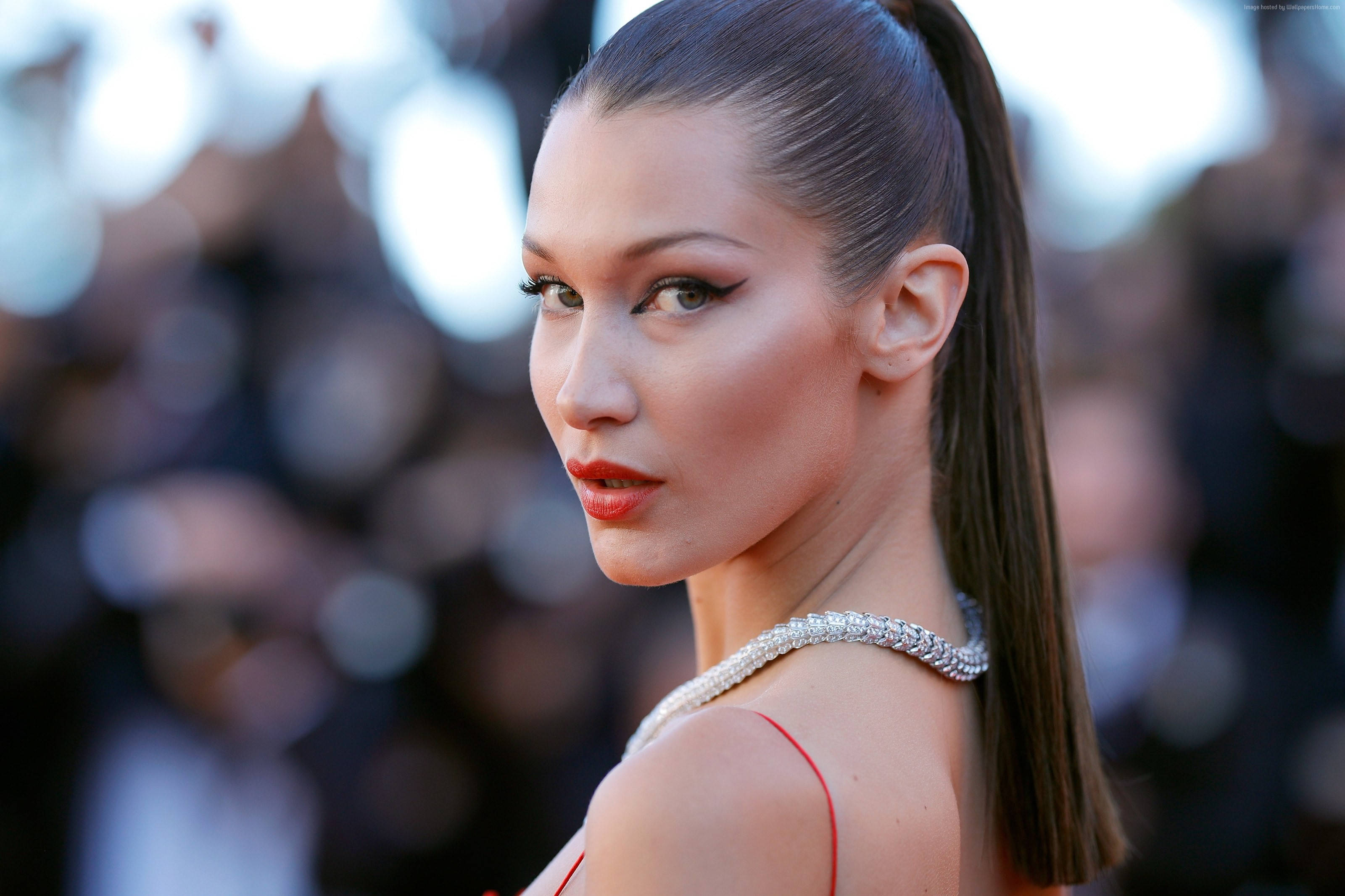 Bella Hadid 桌布 壁紙 — 一位時尚女性，梳著光滑的馬尾辮，塗著大膽的紅唇，在明亮的燈光下自信地在紅地毯活動上擺姿勢。