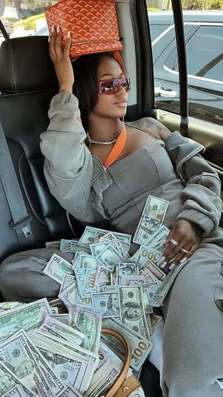 壞女孩美學 桌布 壁紙 — 一位時尚女性在汽車座位上放鬆，周圍散落著現金，頭上頂著一個橙色手袋。