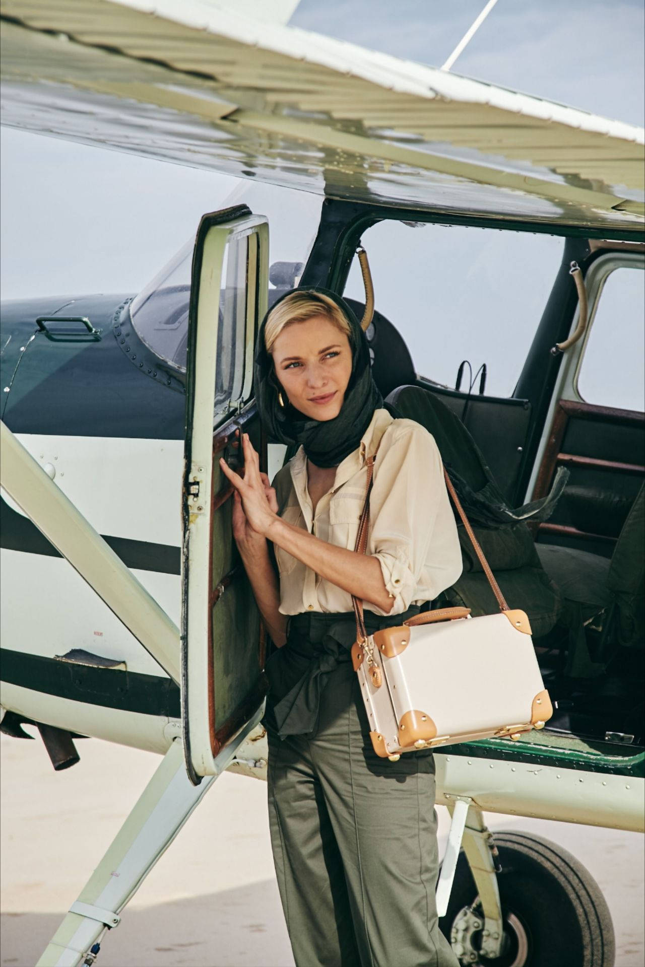 Helicopter 桌布 壁紙 — 一位時尚女性戴著圍巾，拿著復古手提箱，自信地站在小型飛機敞開的門前，在明亮的日光下。