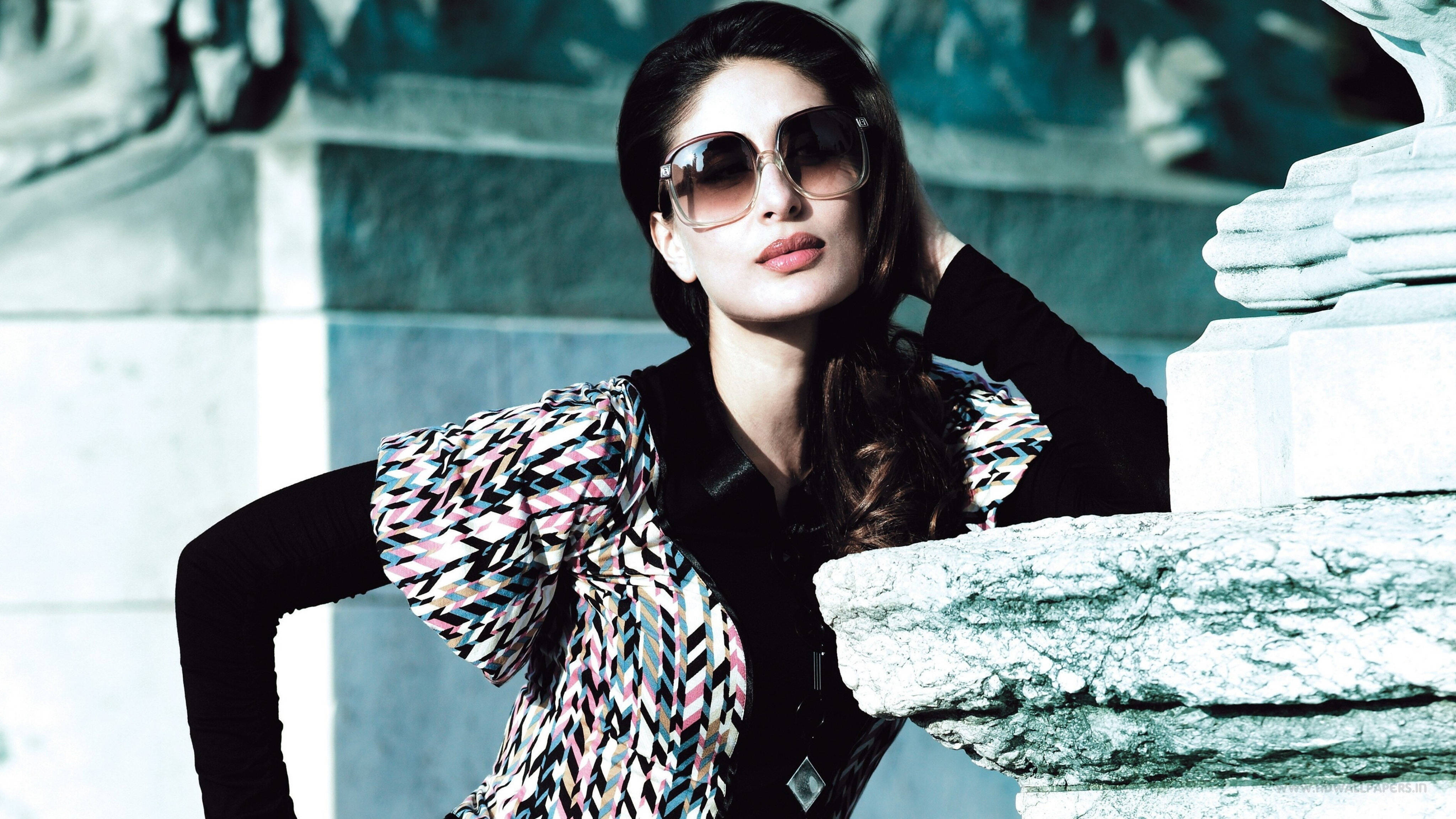 Kareena 桌布 壁紙 — 一位時尚女性戴著超大太陽眼鏡和圖案襯衫，在冷藍燈光下自信地在石紀念碑前擺姿勢。