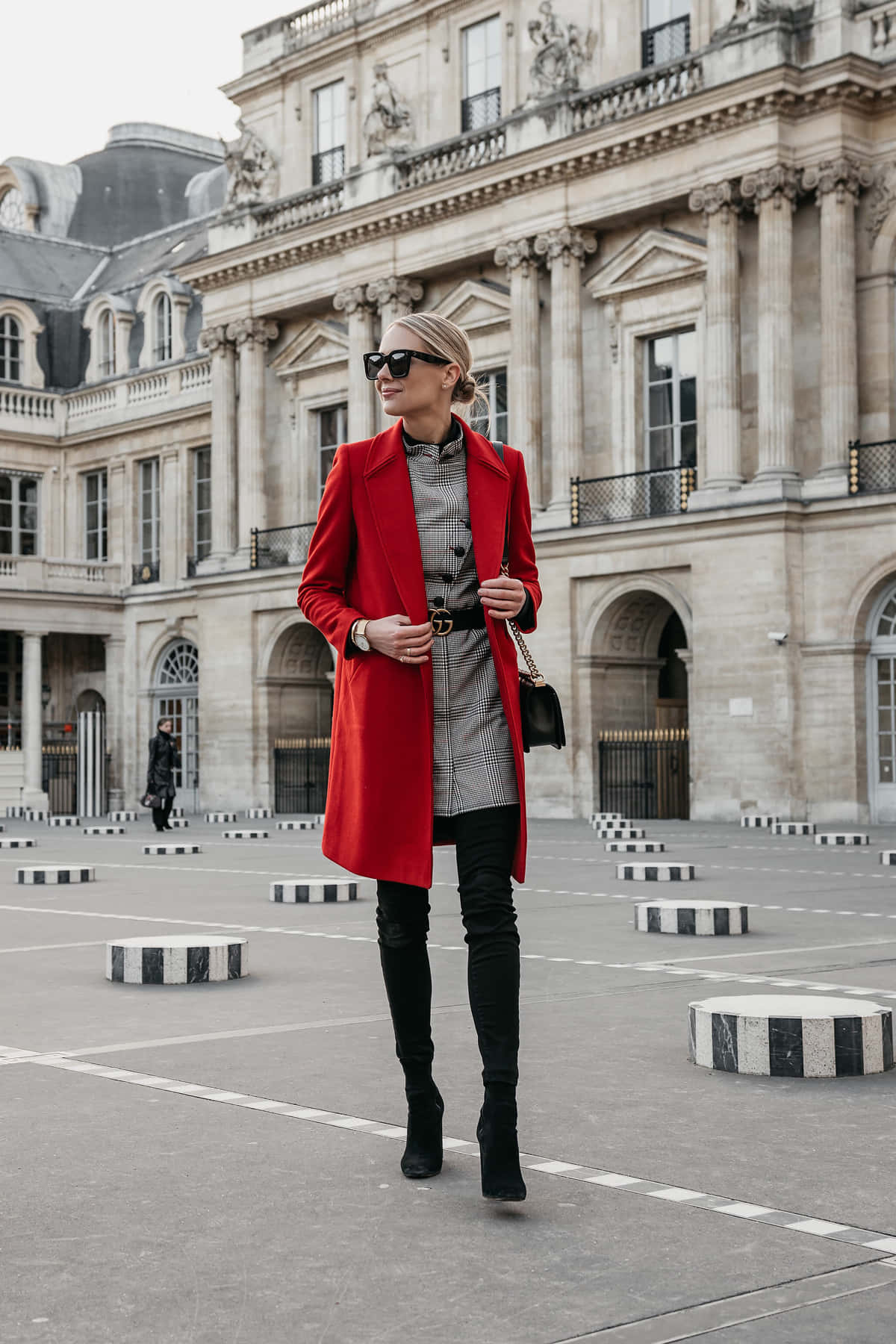 Red Coat 桌布 壁紙 — 一位時尚女性穿著大膽的紅色外套，自信地站在一個擁有古典建築和條紋護柱的宏偉歐洲廣場上。