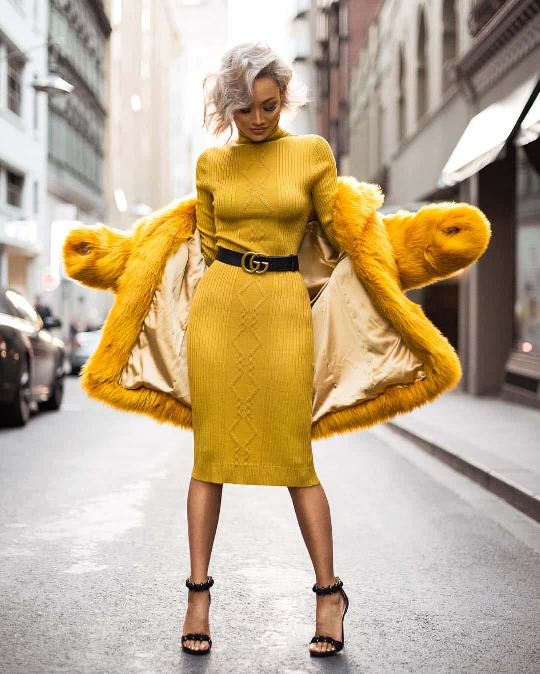 Yellow Fashion 桌布 壁紙 — 一位時尚女性穿著大膽的黃色針織連衣裙和相配的毛邊外套，自信地站在城市街道上。