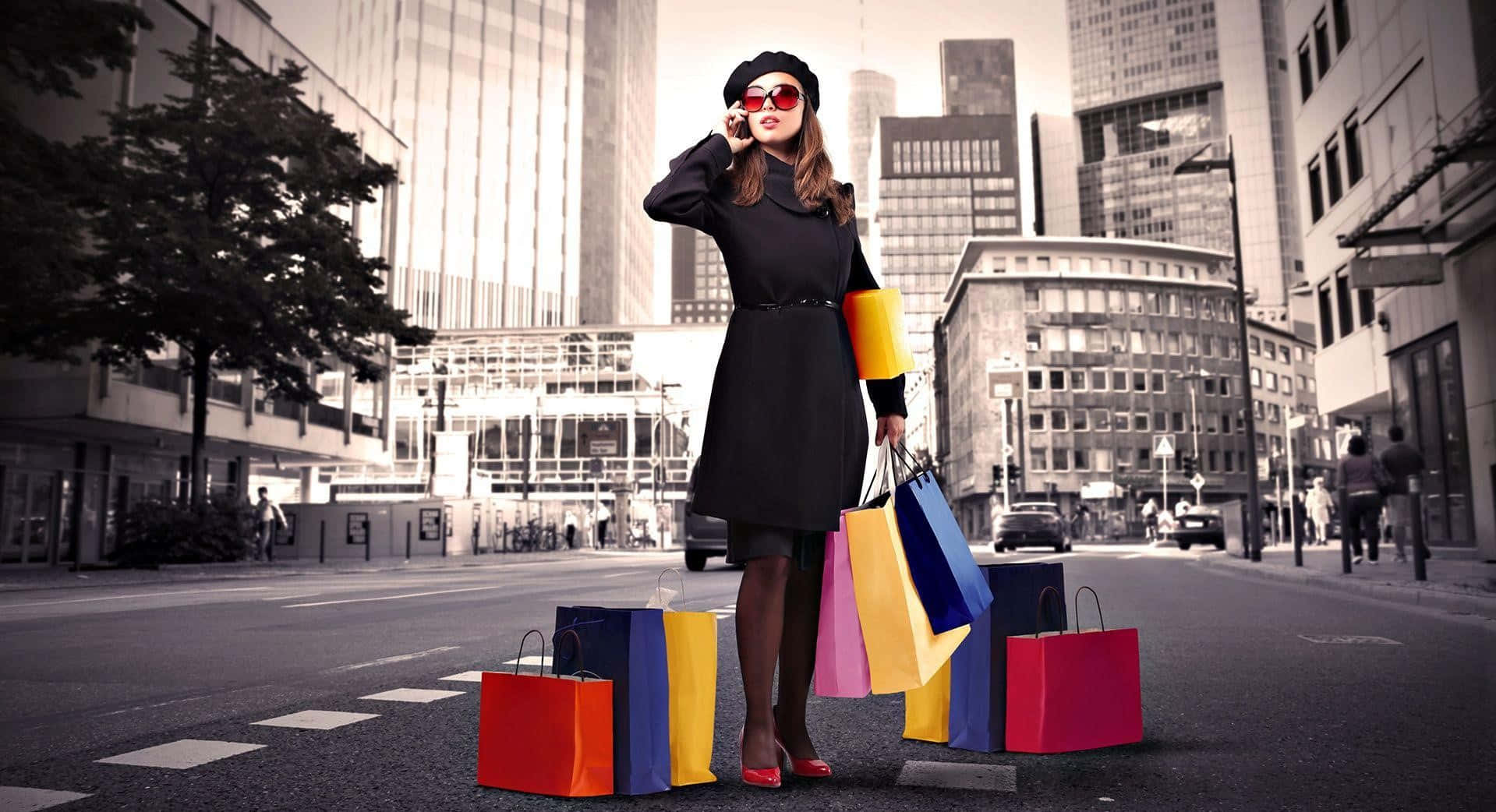 Shopping 桌布 壁紙 — 一位時尚女性穿著黑色連衣裙和紅色太陽眼鏡，站在城市街道上，手持色彩繽紛的購物袋，正在講電話。