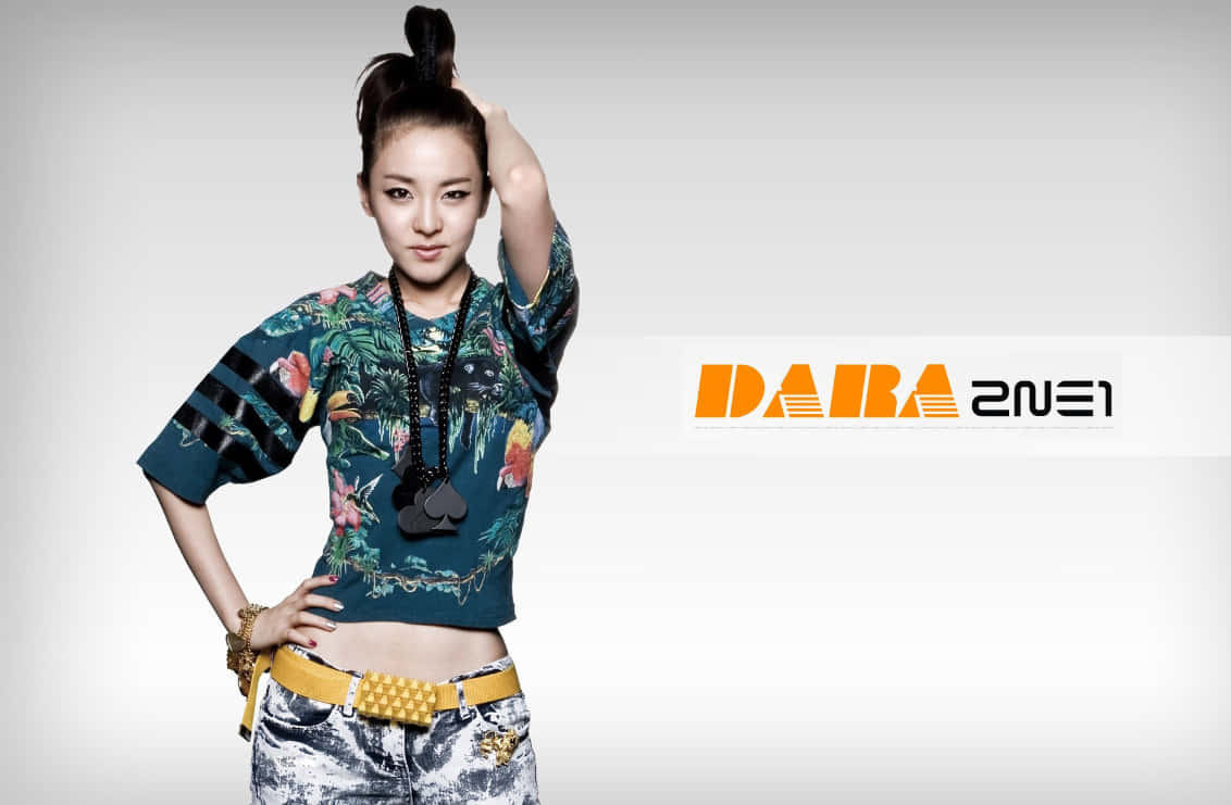 2ne1 桌布 壁紙 — 一位時尚女性紮著高馬尾，穿著熱帶印花短版上衣和鉚釘腰帶，在純灰色背景前自信地擺姿勢。