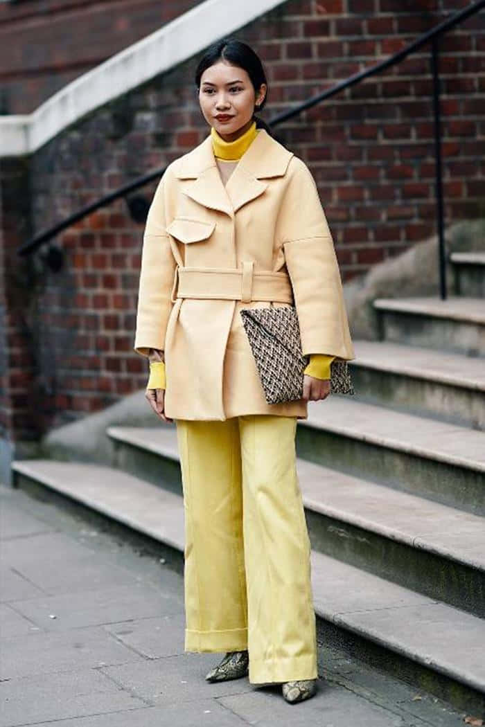 Yellow Fashion 桌布 壁紙 — 一位時尚女性身穿米色外套和黃色褲子，自信地站在城市石階上，背景是磚牆。