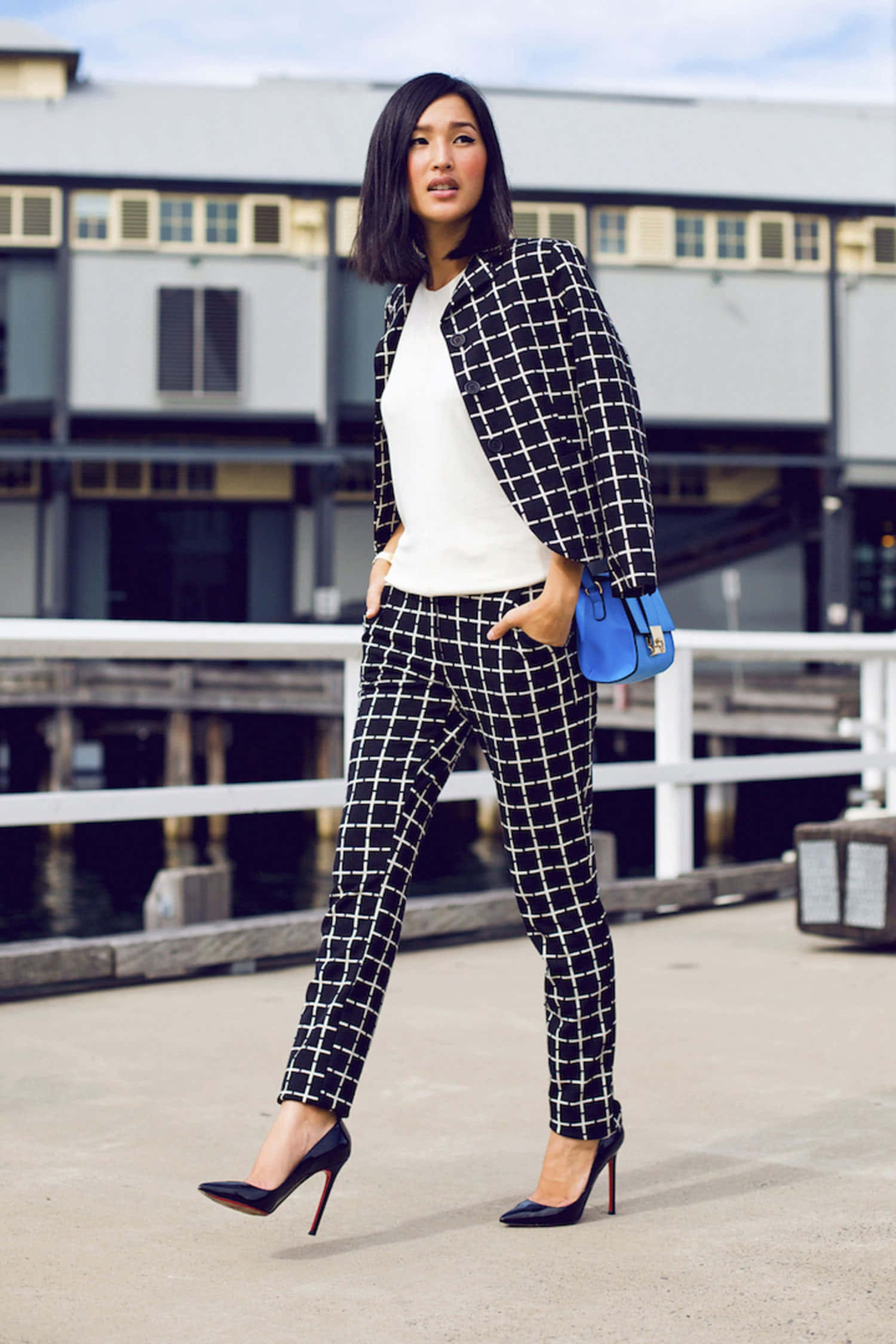 Black And White Fashion 桌布 壁紙 — 一位時尚女性身穿黑白格紋西裝，自信地站在海濱碼頭，手持藍色手提包。