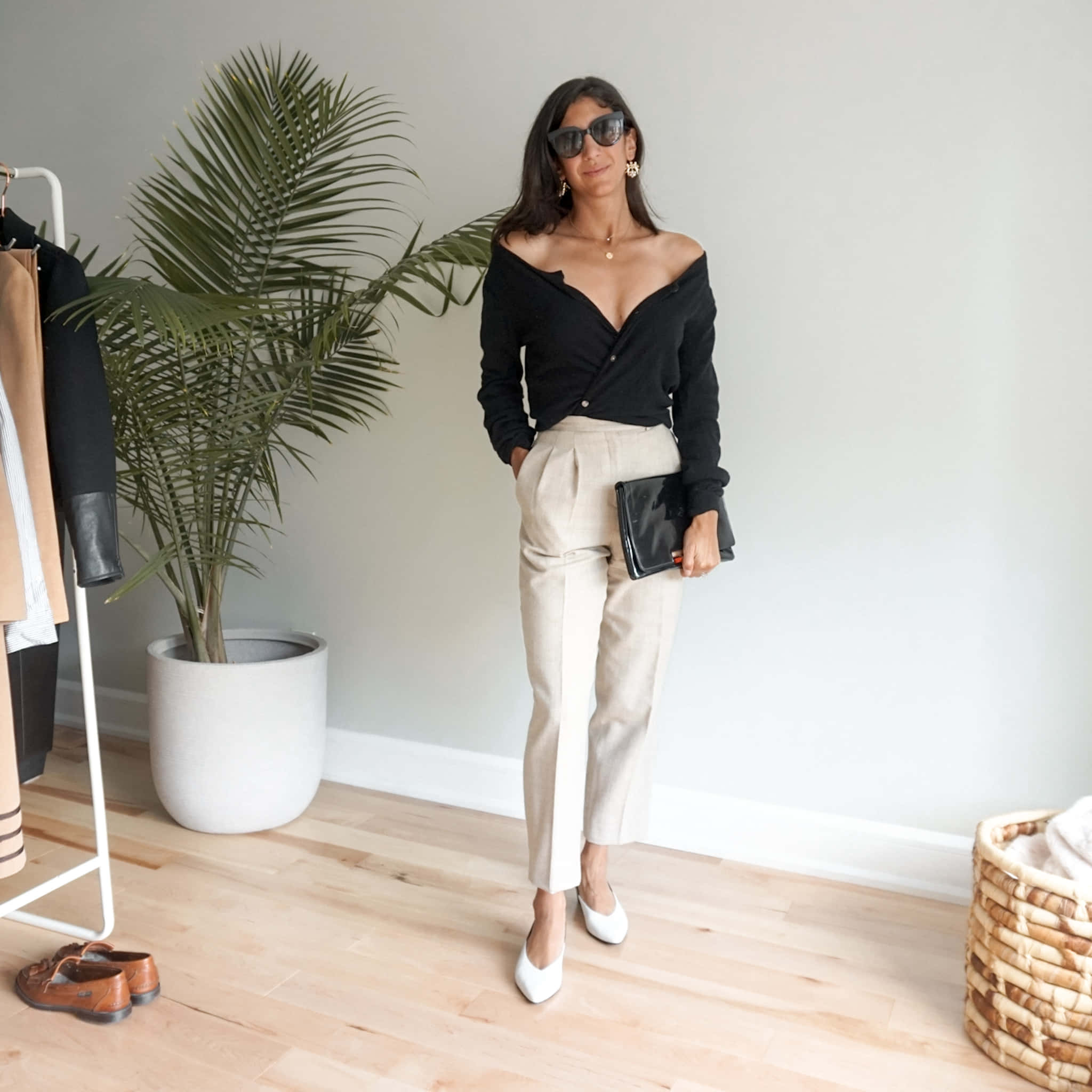 Minimalist Fashion 桌布 壁紙 — 一位時尚女性身穿黑色露肩上衣和米色長褲，在一個有盆栽棕櫚樹和木地板的簡約房間裡自信地擺姿勢。
